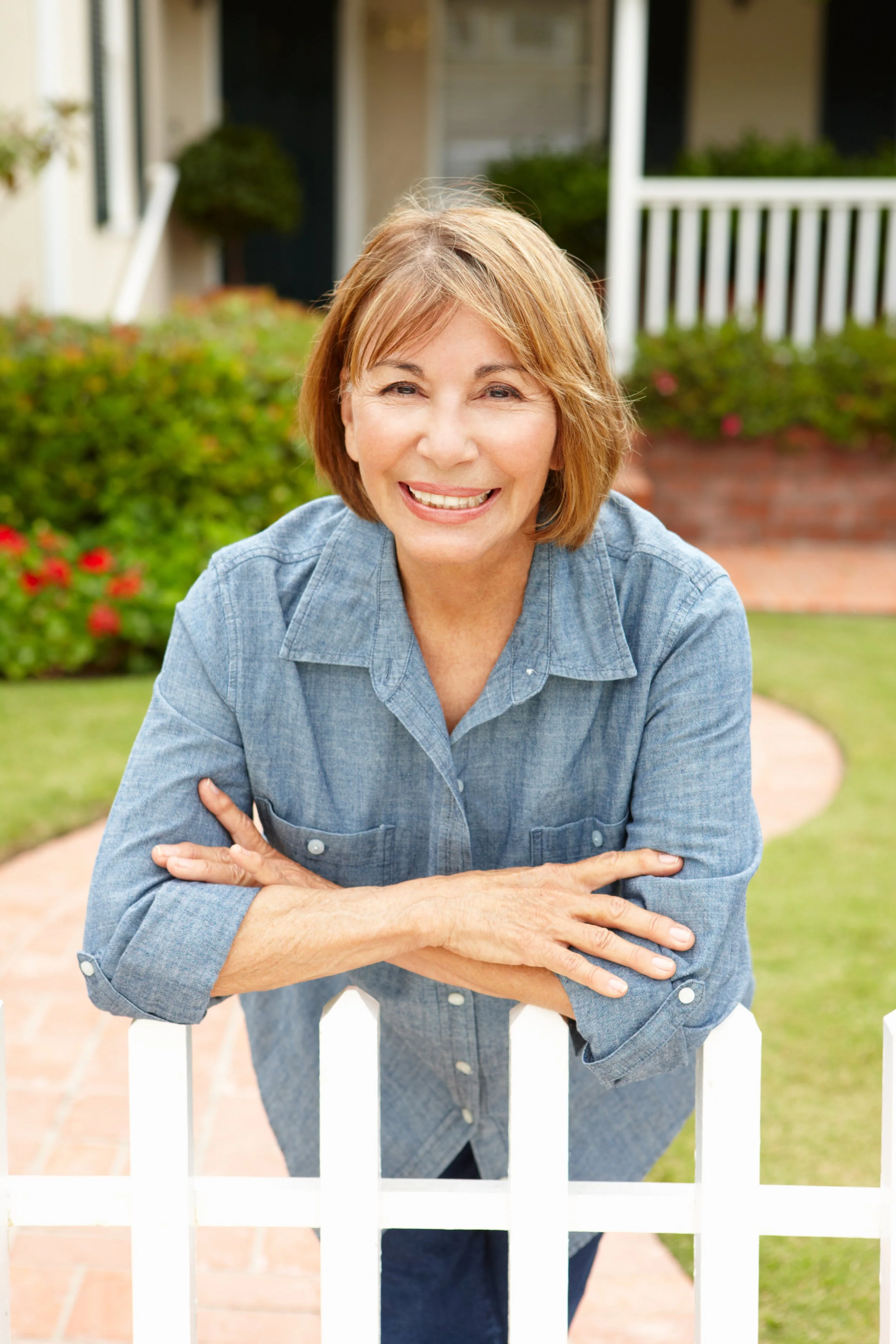 Smiling woman leaning on a white picket fence in a garden