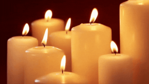 Multiple lit candles with flickering flames against a dark background.