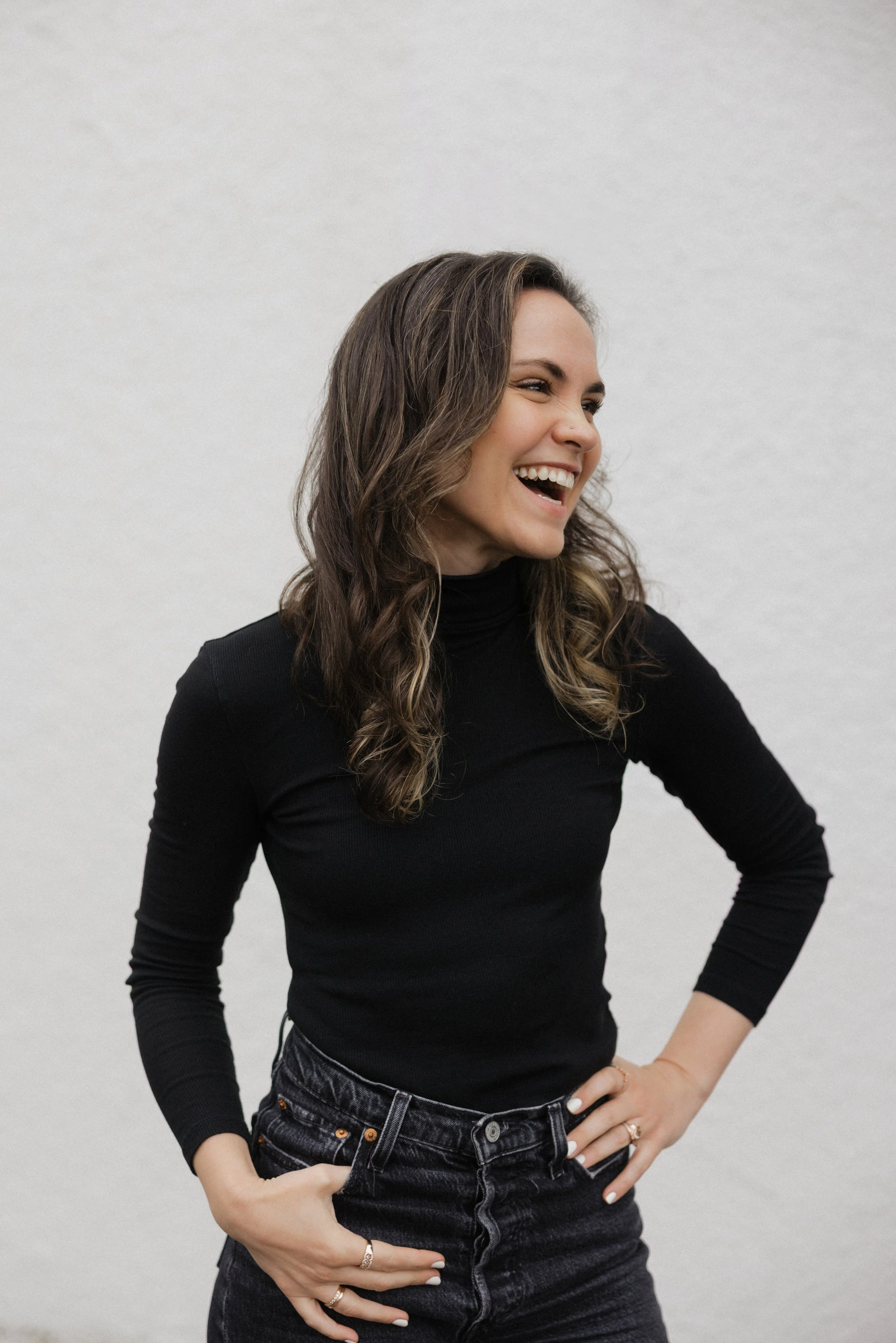Lynnette Oss Connell, a burnout coach, workshop leader, and keynote speaker, stands against a white wall, smiling and laughing as she gazes into the distance.
