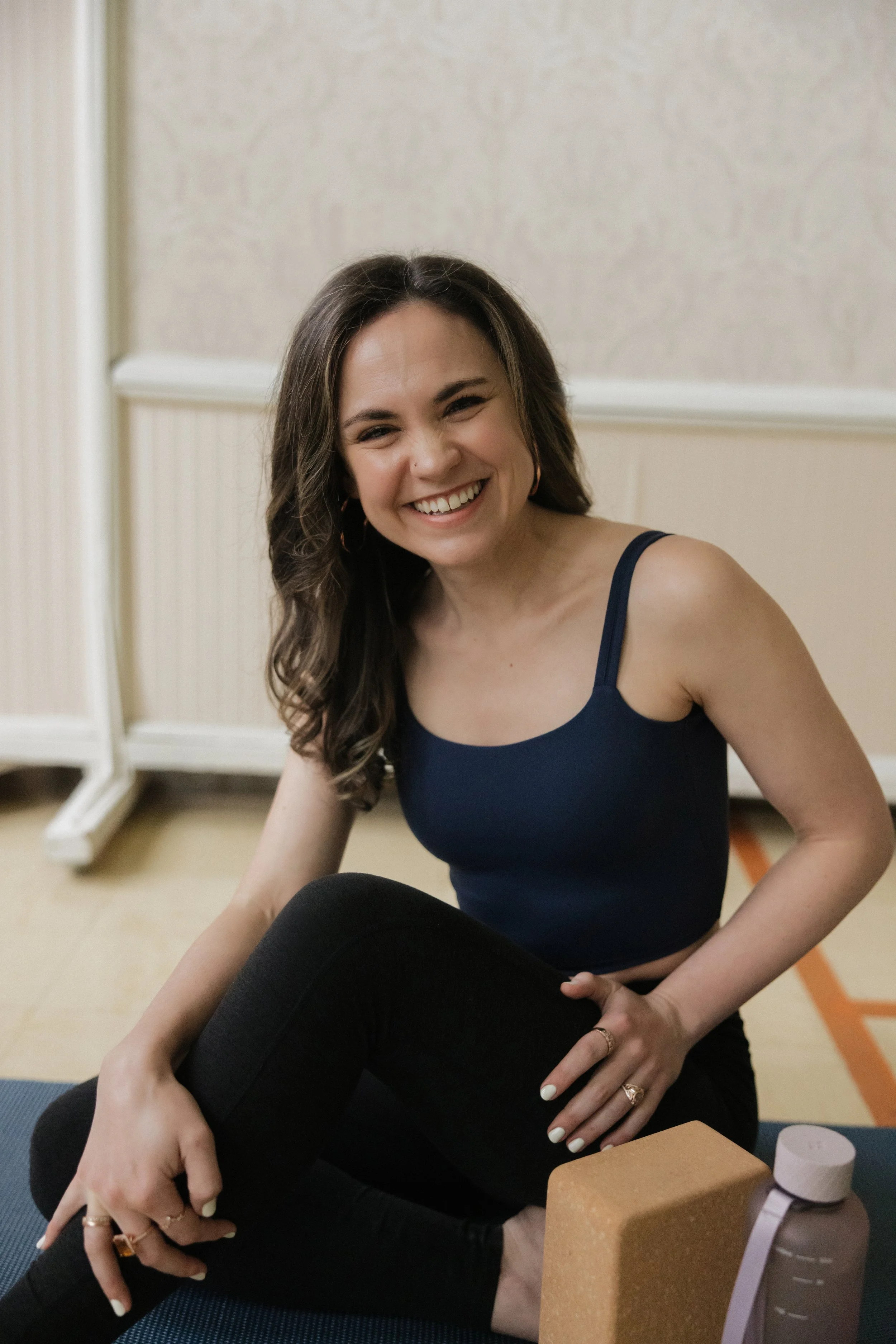 Lynnette Oss Connell, burnout coach, workshop leader, and keynote speaker, sits joyfully smilling cross-legged on the floor during a yoga session.