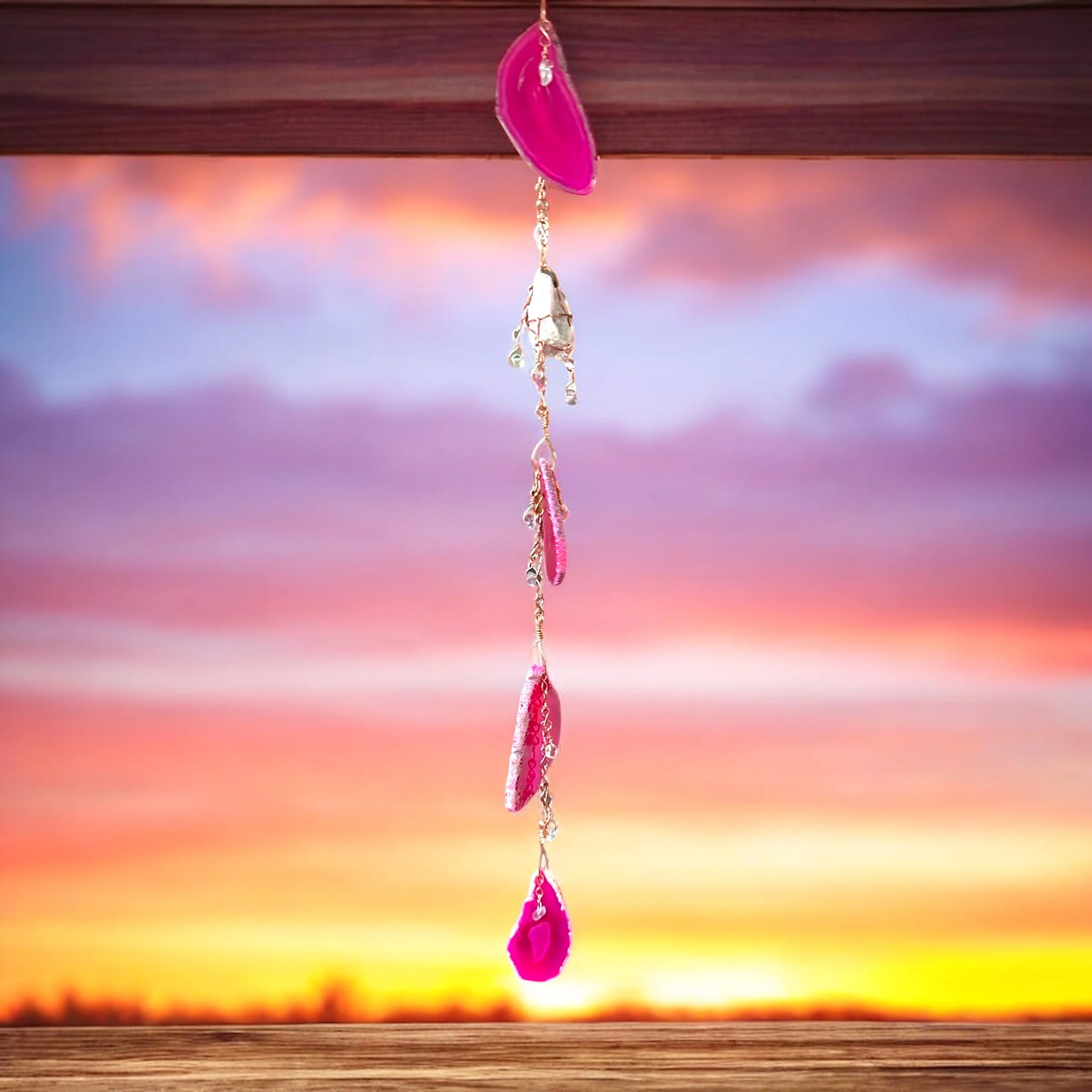 Pink and silver wind chime hanging against a colorful sunset sky.
