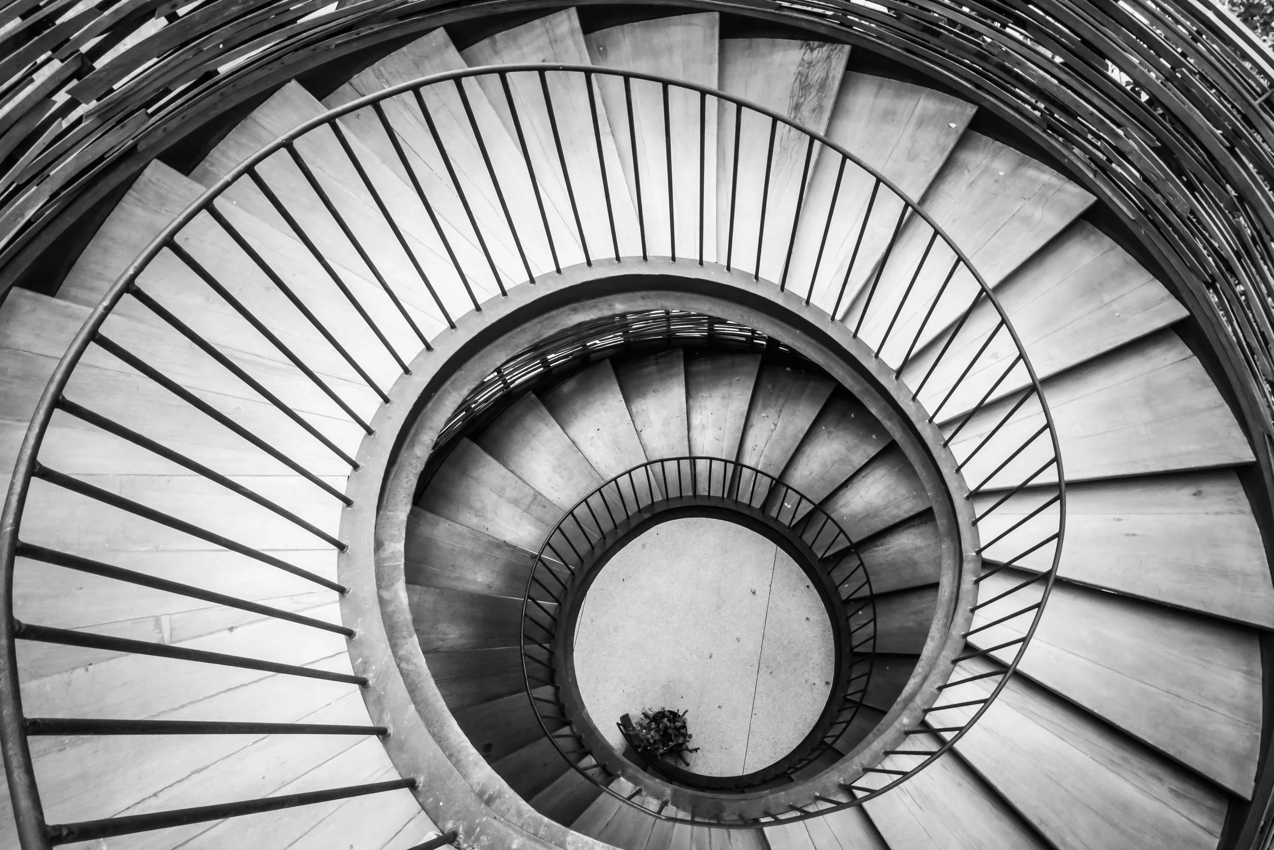 Black and white photo of a spiral staircase viewed from above, with wooden steps and metal railings.