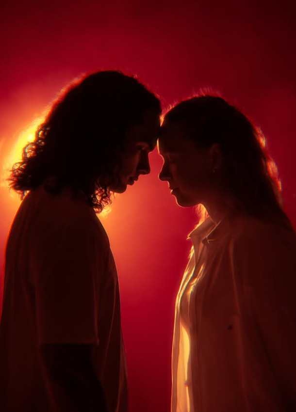 Silhouette of a couple with foreheads touching, backlit by a red and orange light.