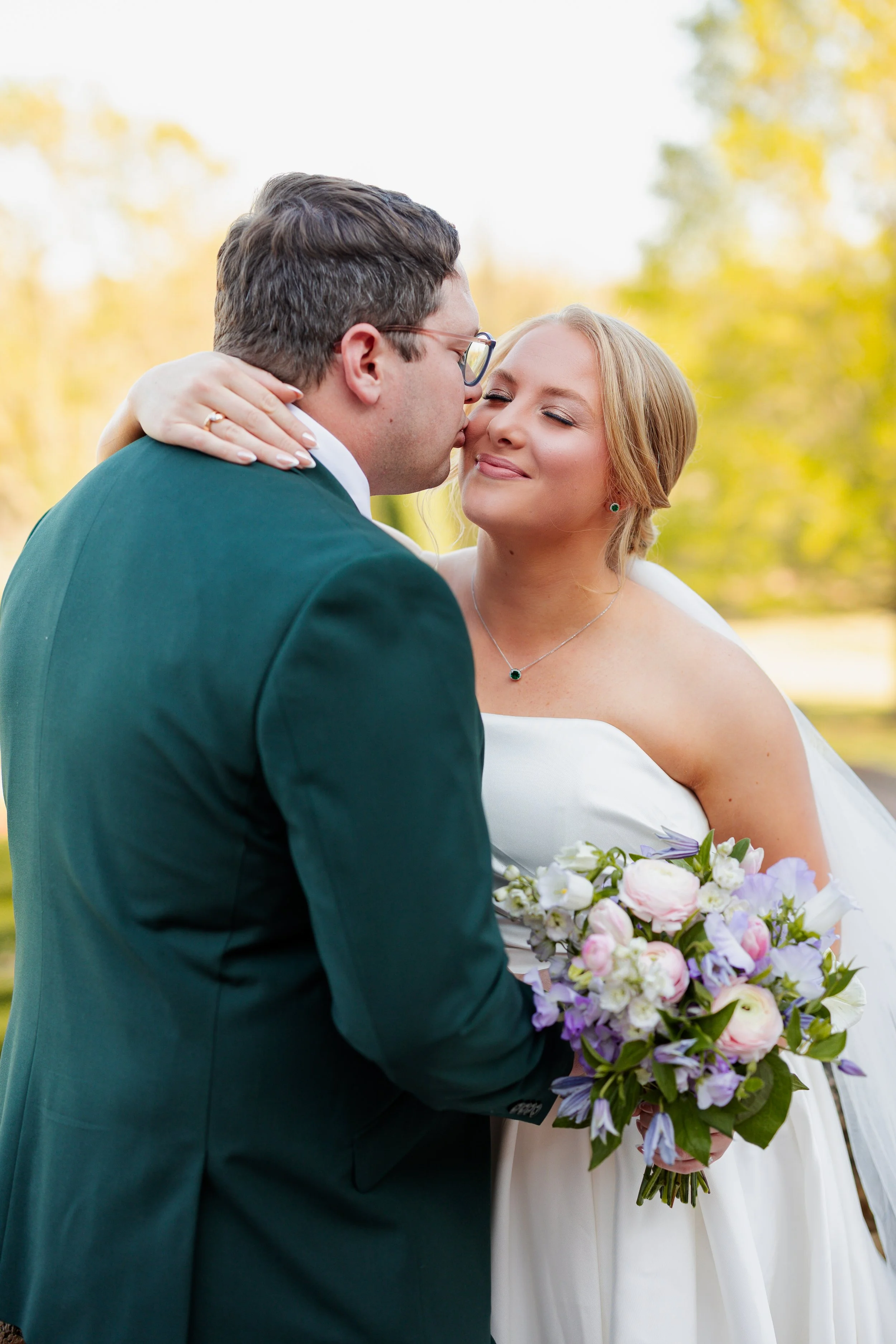 bride and groom share a kiss while holding spring bouquet