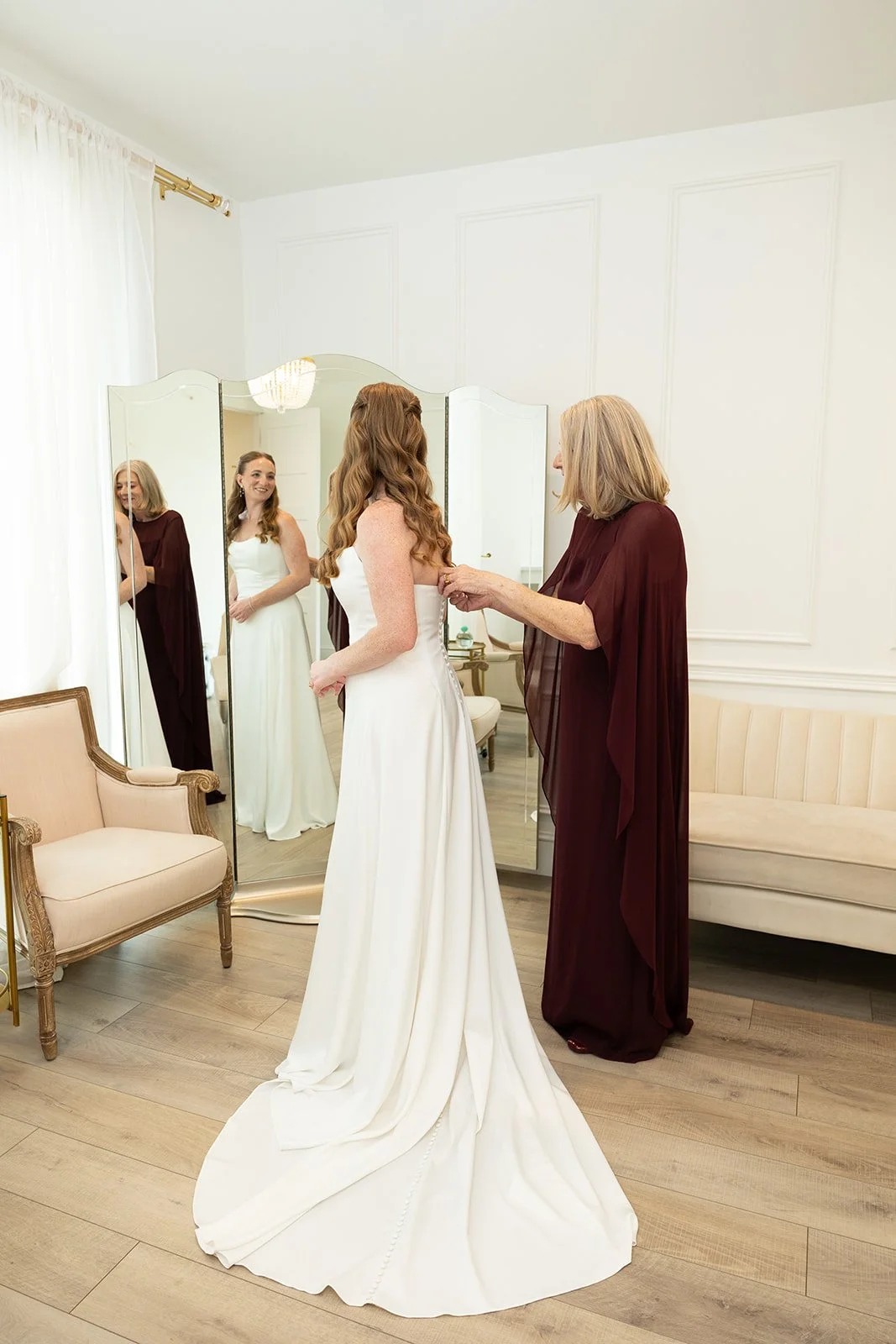 her gown being fastened in the getting-ready room, her smile caught in the mirror · source: Details + Getting Ready, details_11