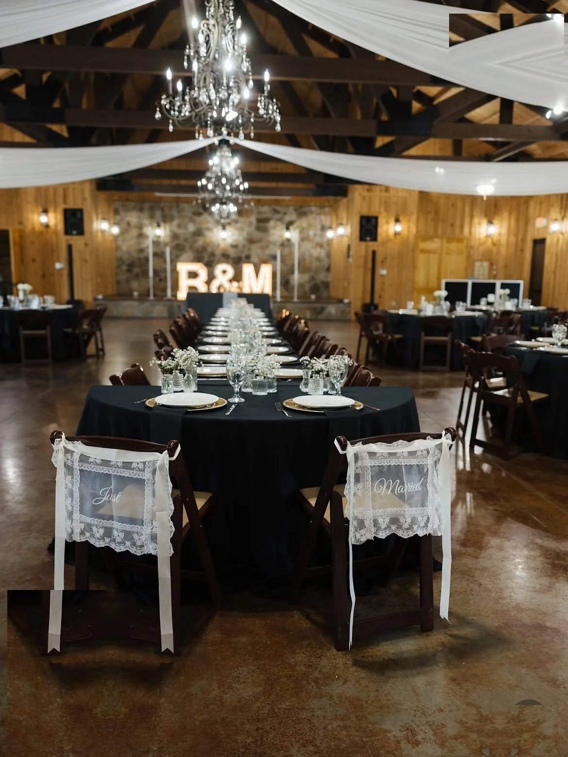 Wedding reception hall with long tables, black linens and illuminated R&M marquee letters