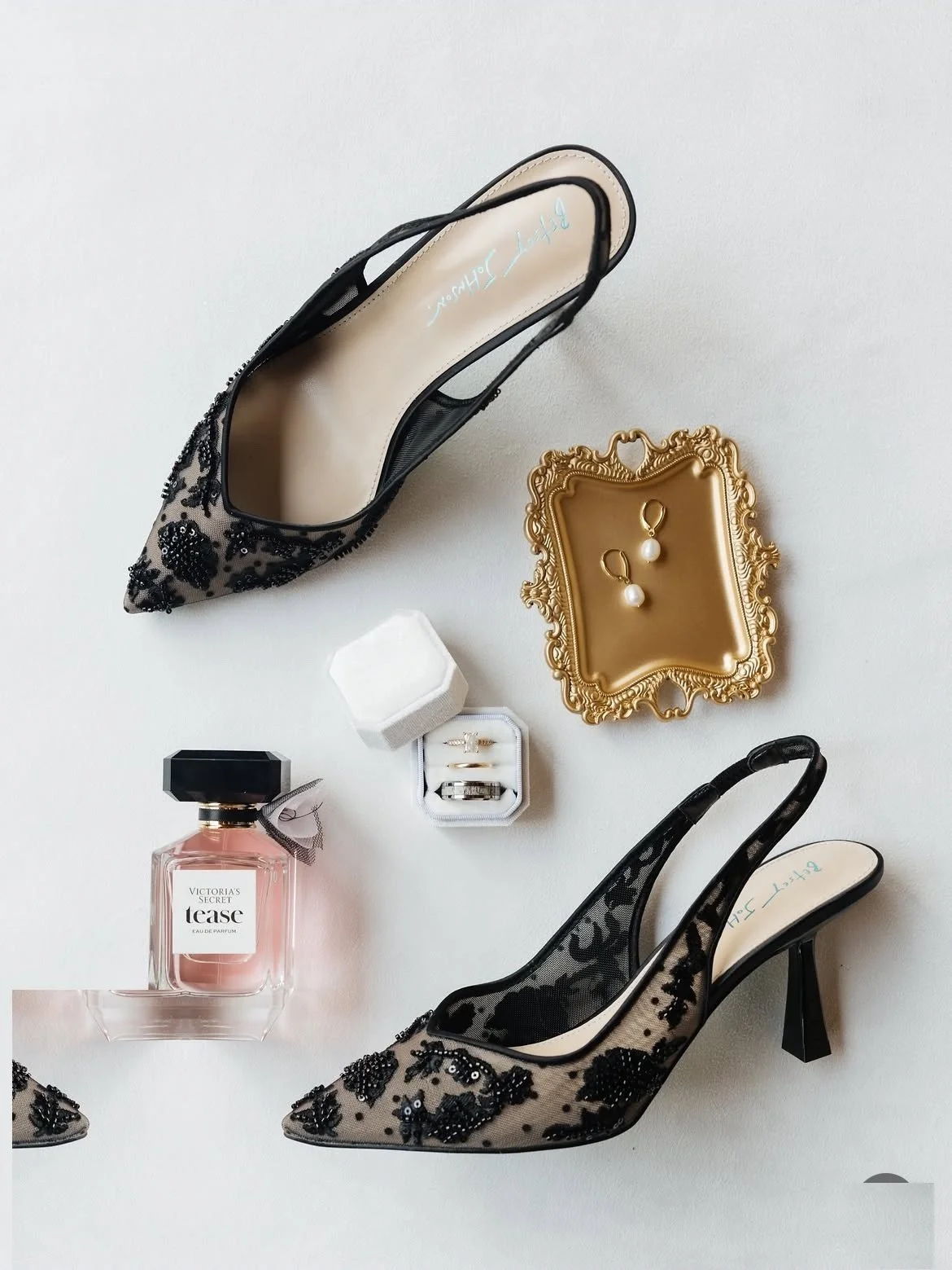 Wedding day details — black lace heels, perfume, rings and gold earrings flat lay