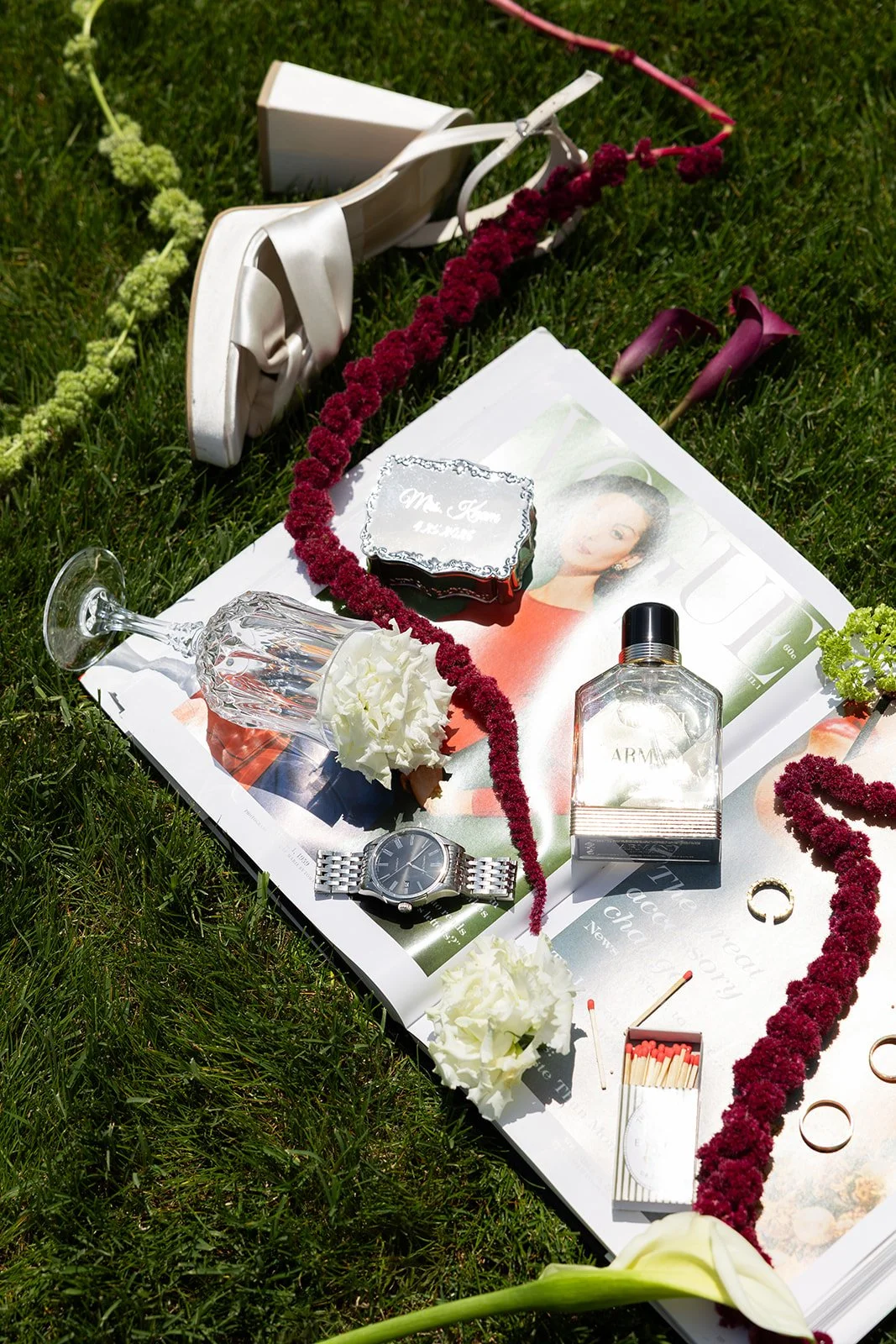  flat lay on the grass — rings, perfume, and the burgundy calla lilies · source: Details + Getting READY