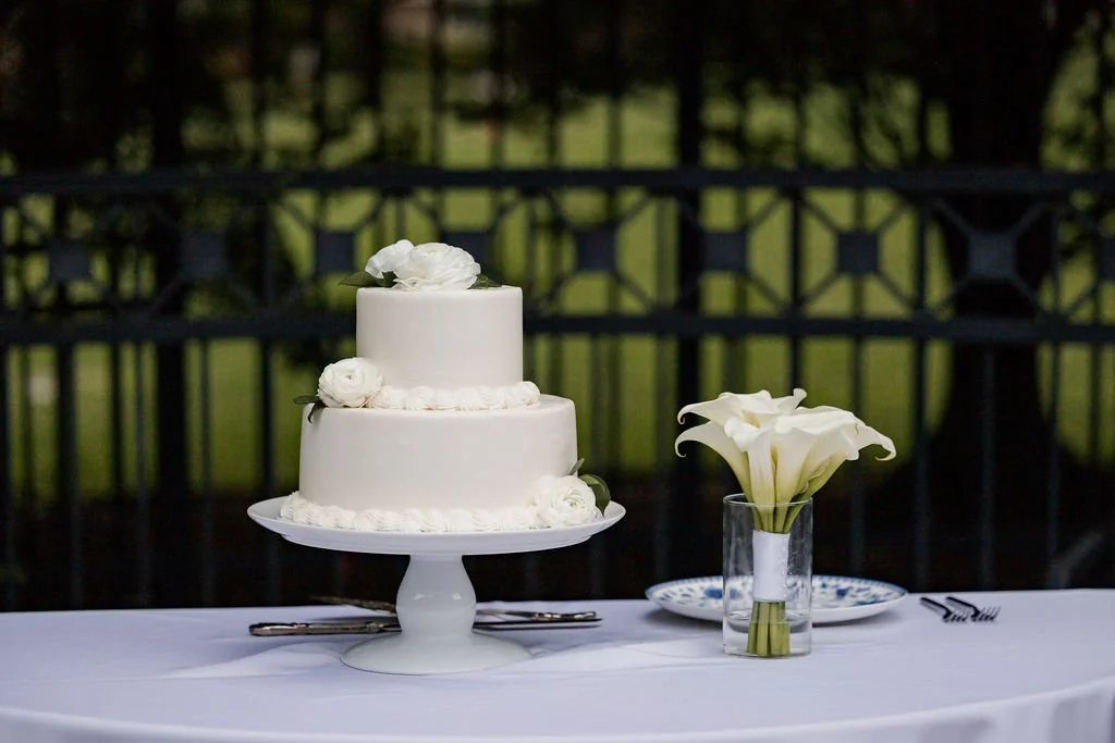 Two-tier white wedding cake with white roses on a pedestal stand, styled cake table