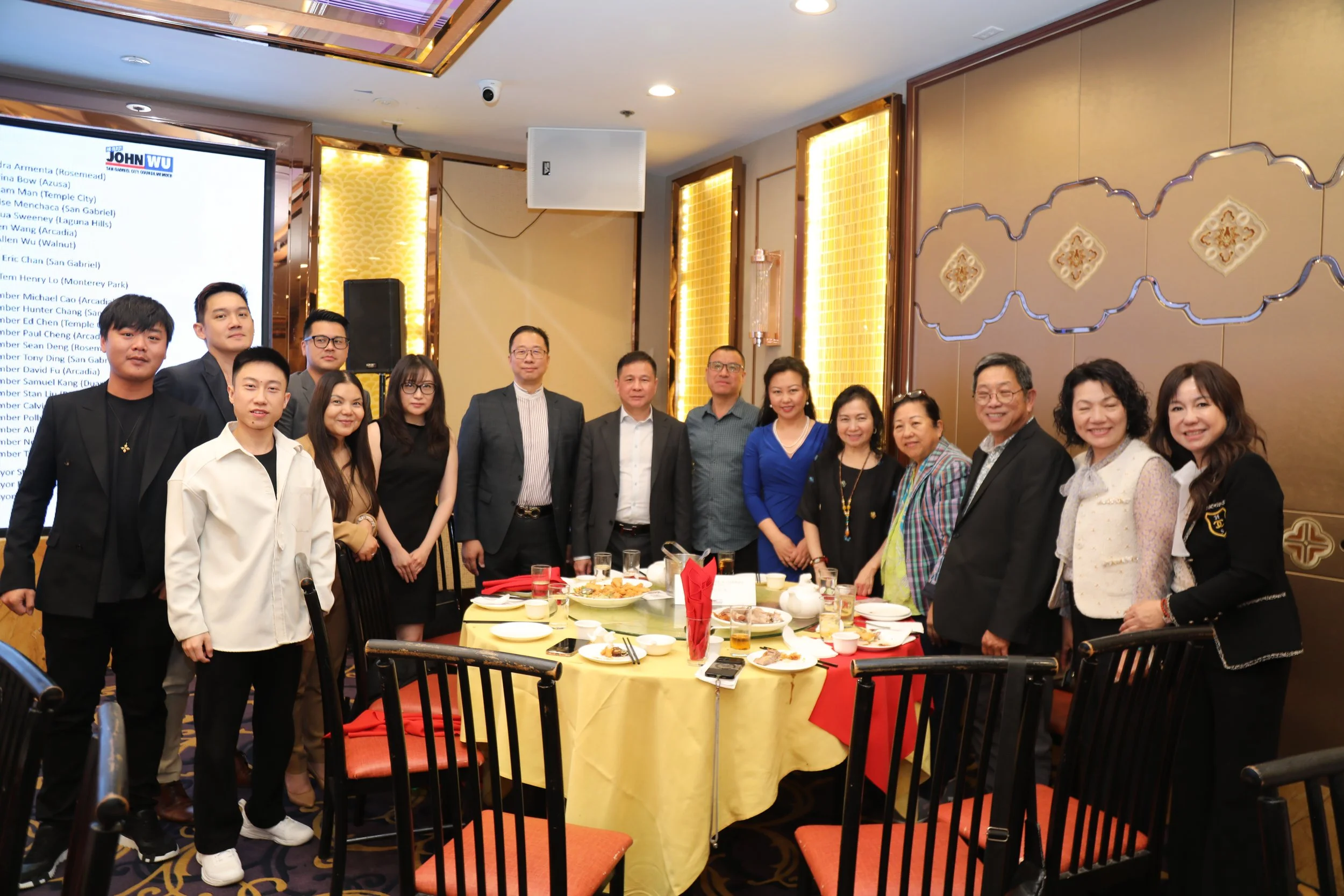 A group of people standing together in a banquet hall or conference room, with a table of food in front of them, celebrating or attending an event.