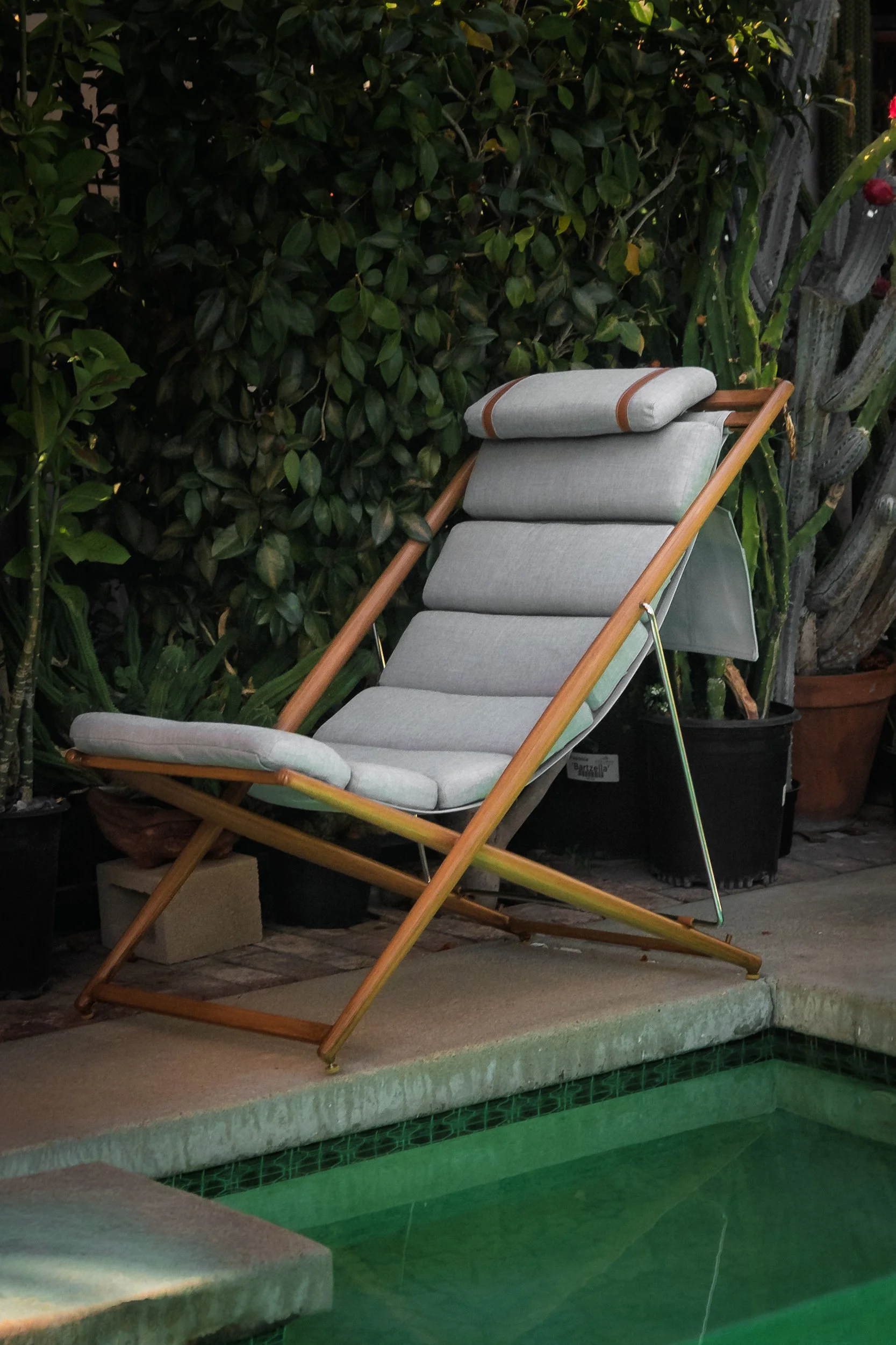 Vertical shot of the Solaris sling chair at the edge of a green pool with plants and cactus behind it