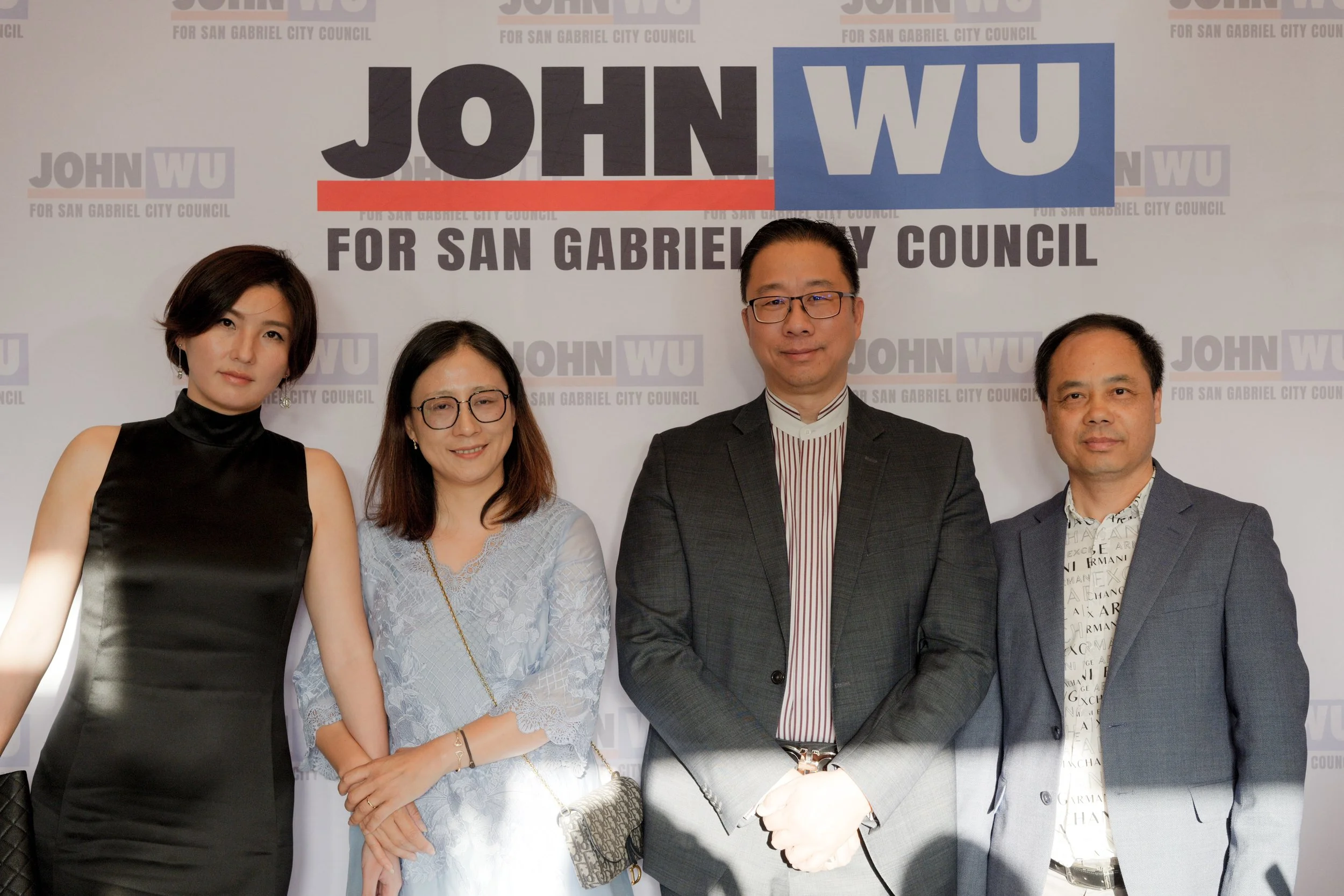 Group of four diverse individuals standing in front of a campaign backdrop that reads 'JOHN WU FOR SAN GABRIEL CITY COUNCIL'.