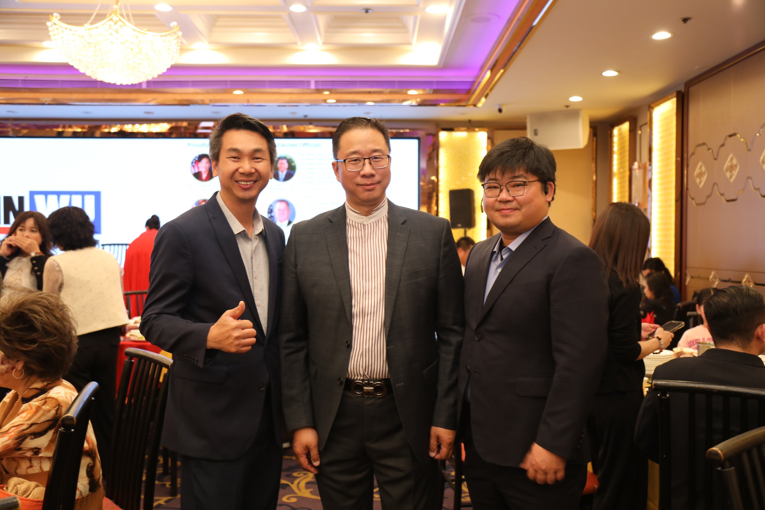 Three men in suits smiling at the camera at a formal event or conference.
