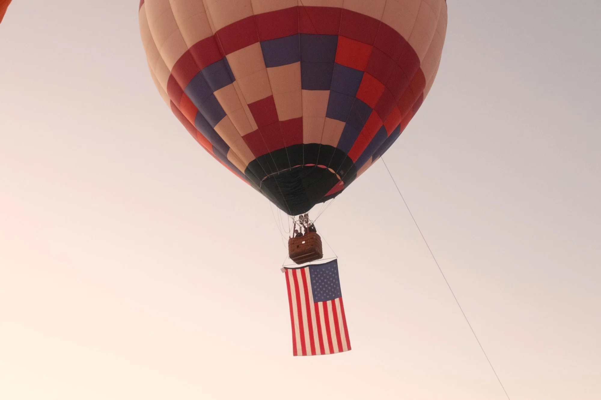 A hot air balloon carrying an American flag in the soft dawn sky