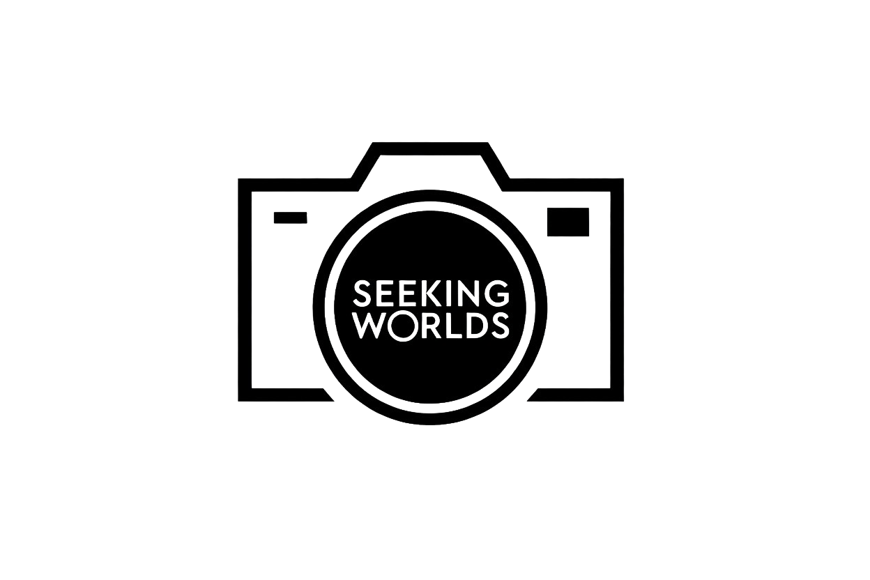 A stylized black and white icon of a camera with the words 'Seeking Worlds' inside the lens.