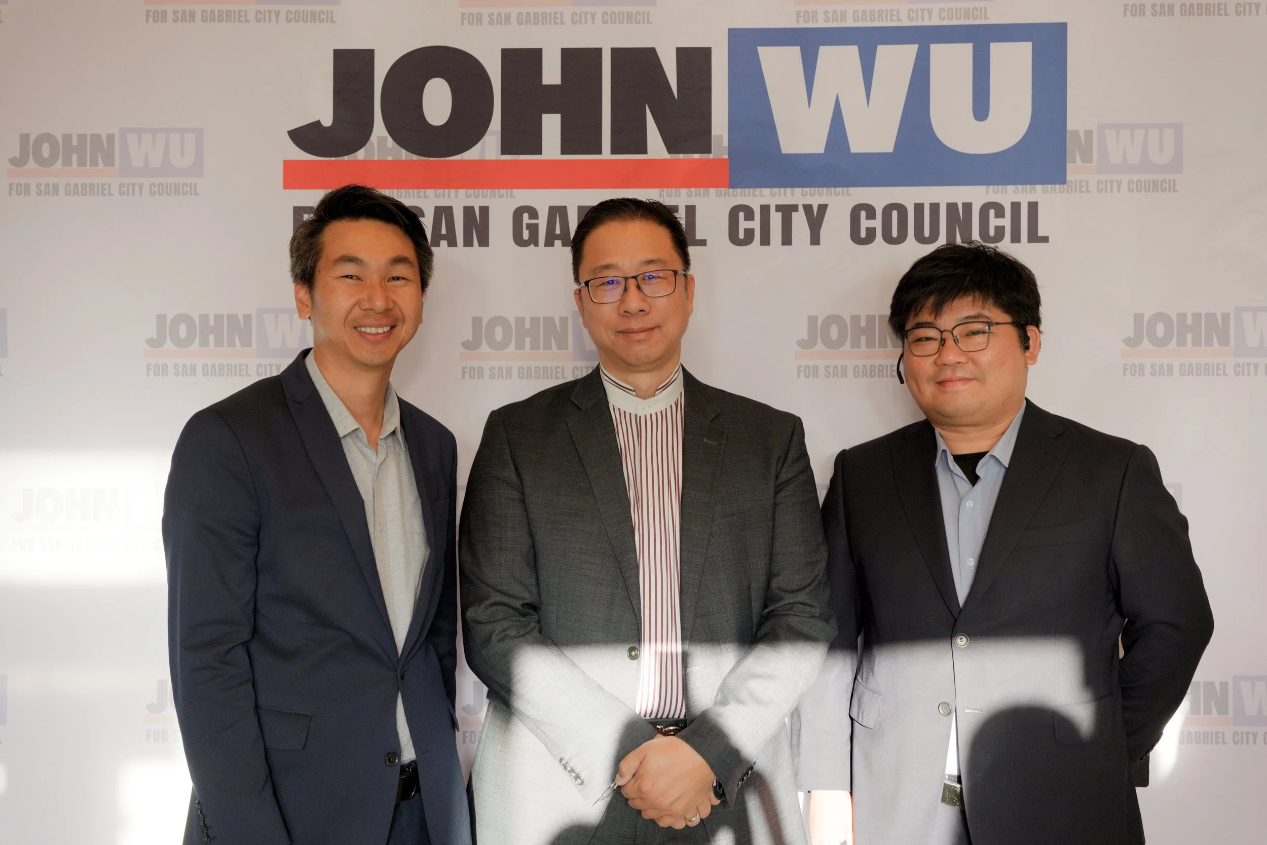 Three men in suits standing together at an event with a backdrop that reads 'JOHN WU FOR SAN GABRIEL CITY COUNCIL' in large letters.