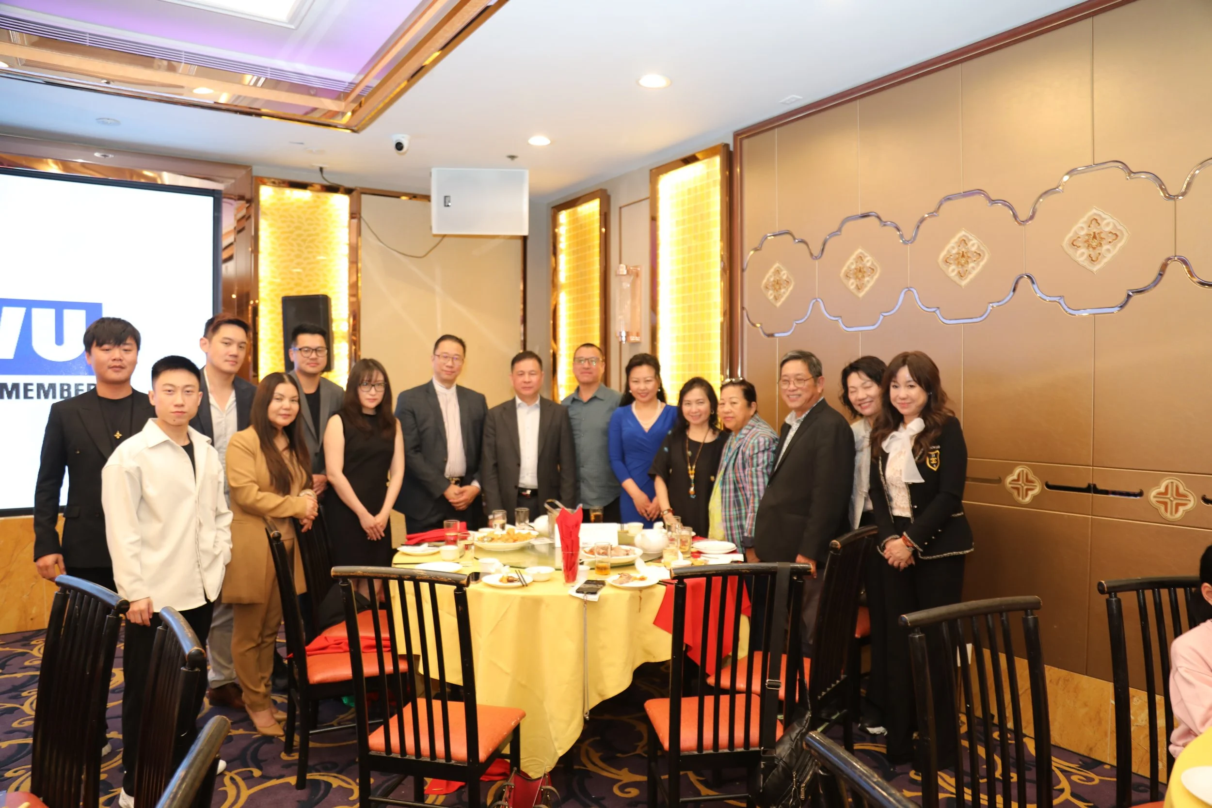 Group of people in formal attire standing around a banquet table at an indoor celebration event.