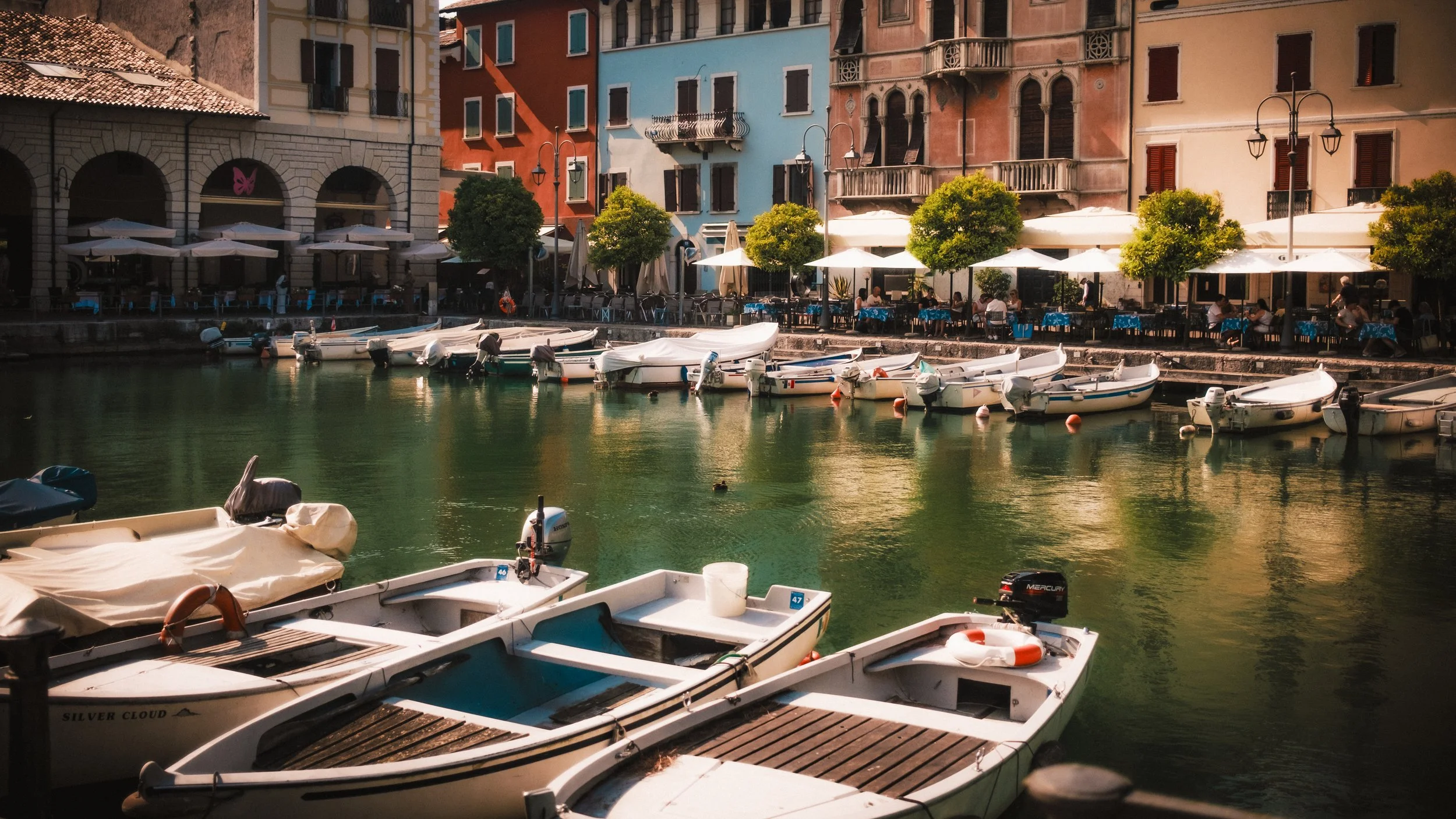 Boats docked along a canal with colorful buildings and outdoor cafes in the background.