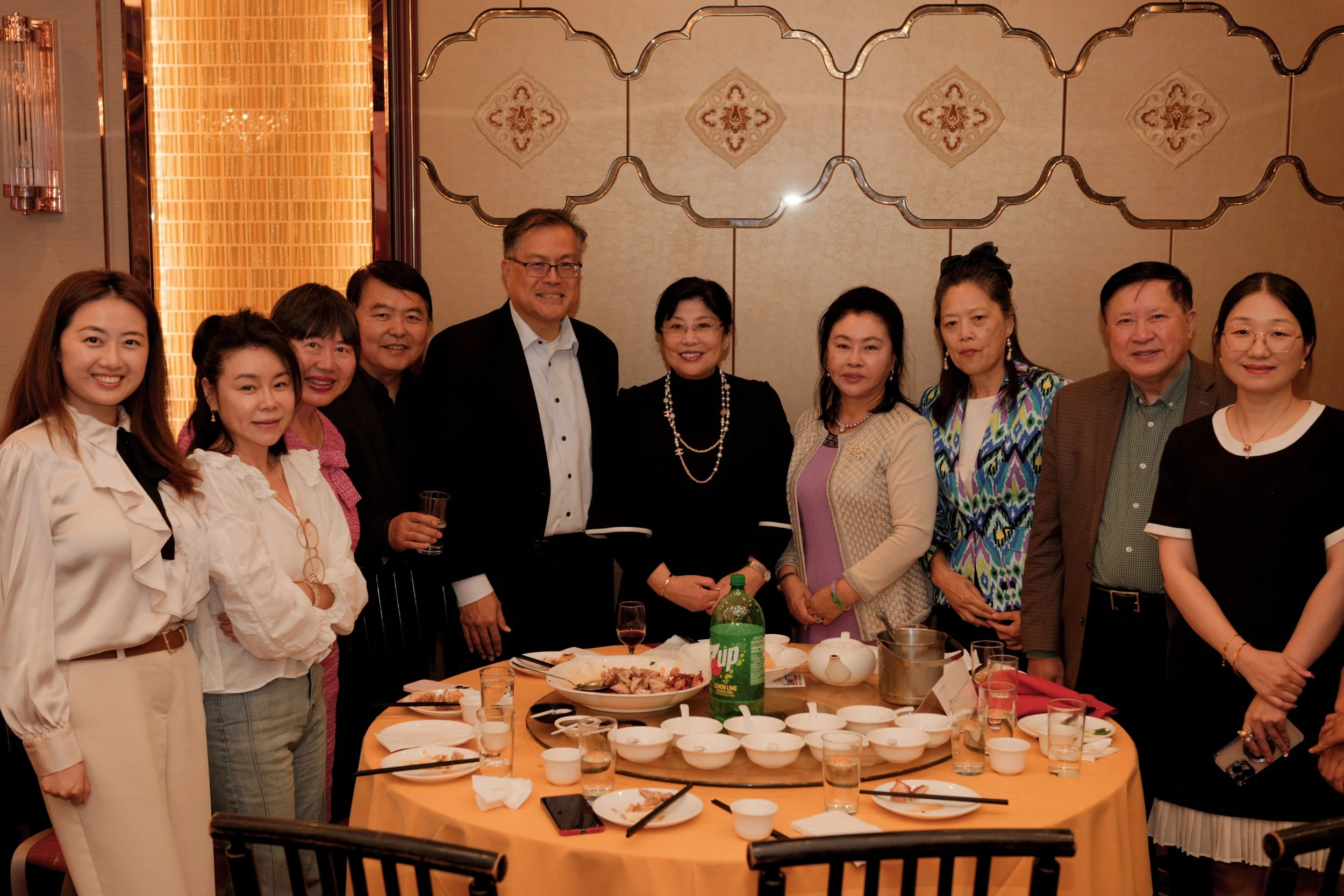 A group of people standing around a dining table at a party or celebration, with food and drinks on the table.
