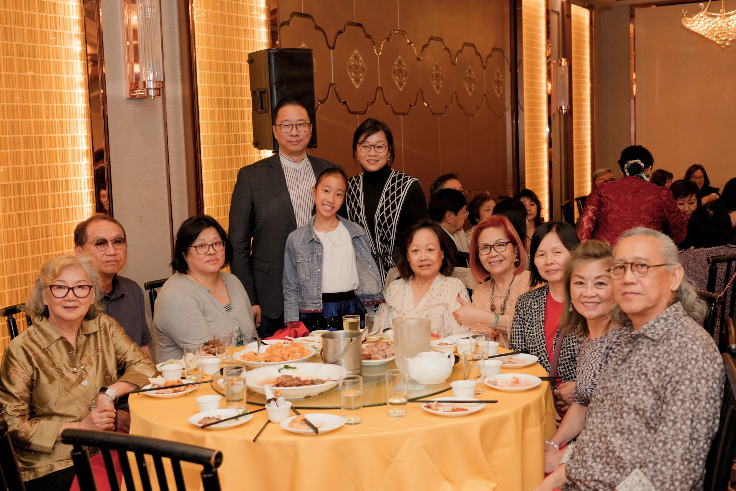 People gathered around a banquet table at an event, with food and drinks, set in a decorated banquet hall.