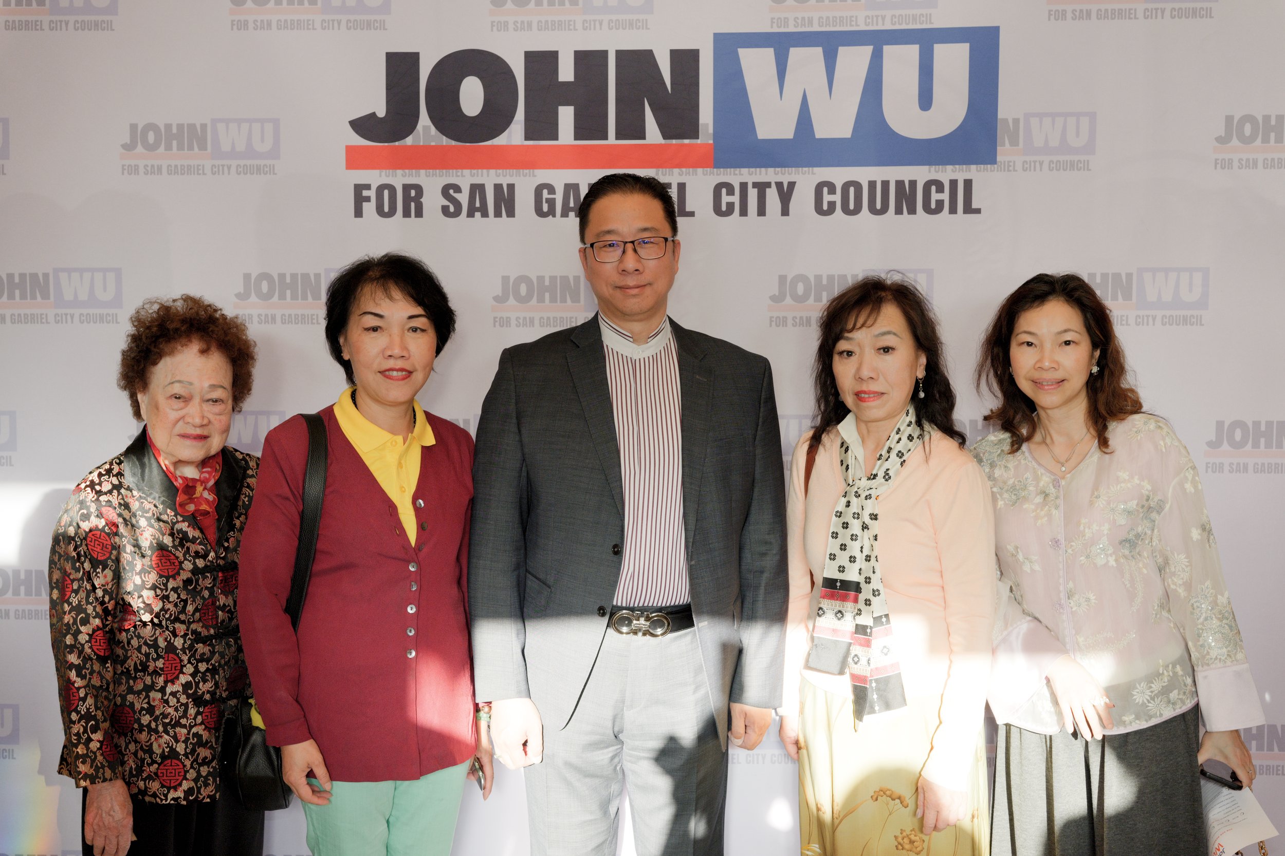 Group of six people standing in front of a politically branded backdrop promoting a candidate for San Gabriel City Council, including one man in a suit and five women.