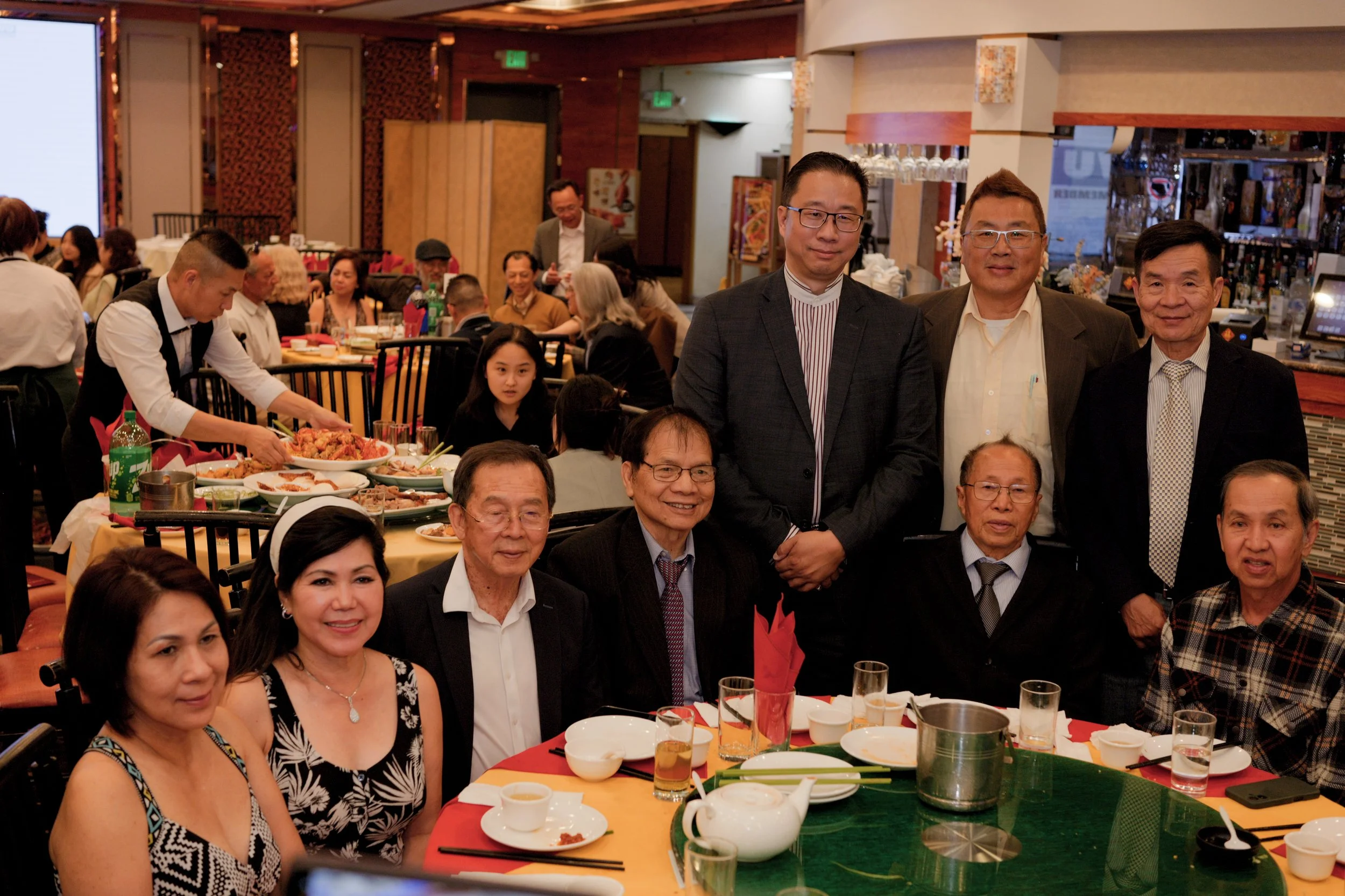 A group of people gathered in a restaurant for a celebration, with food on the table and some individuals posing for a photo.