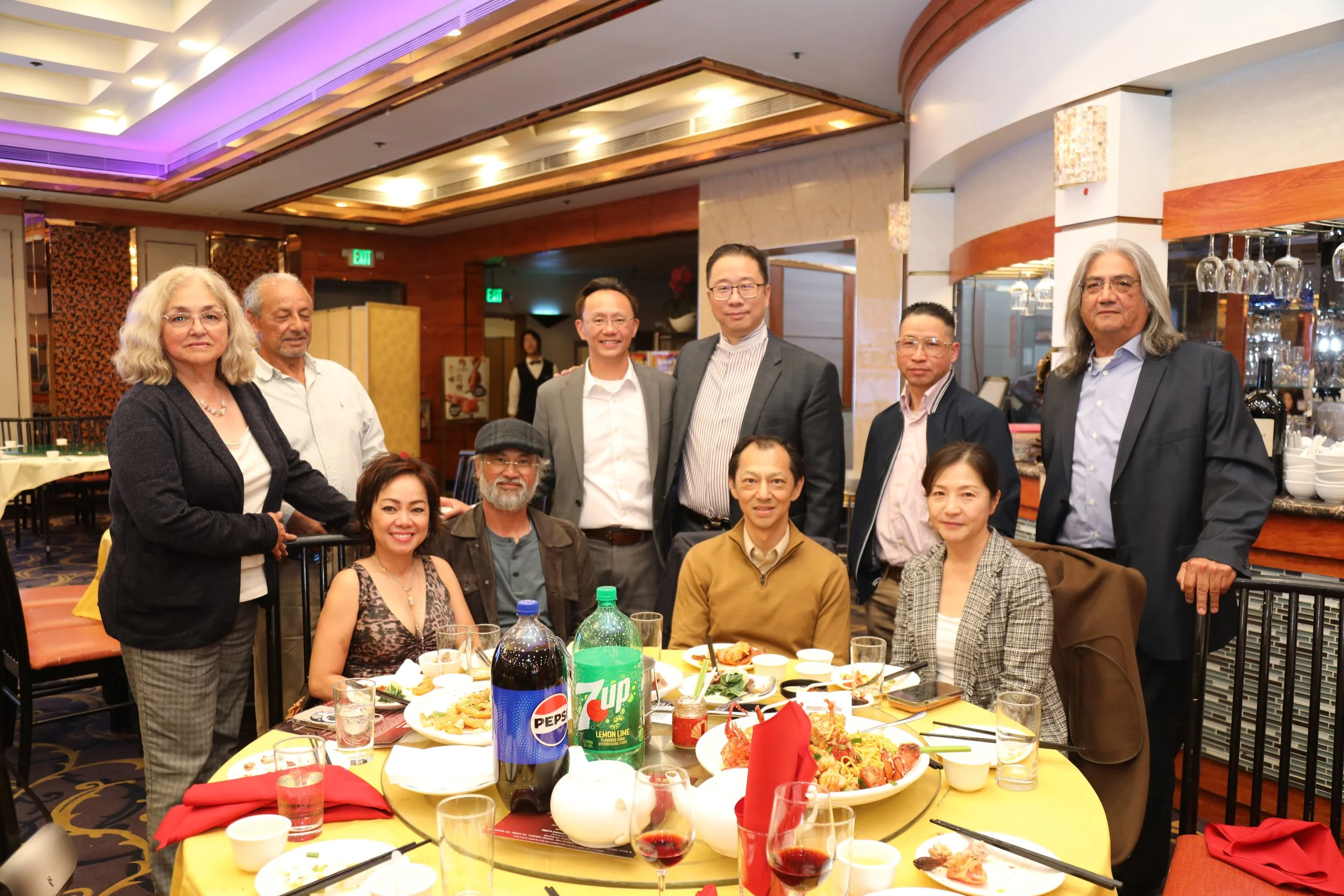 Group of people gathered at a restaurant for a celebration, with food and drinks on the table.