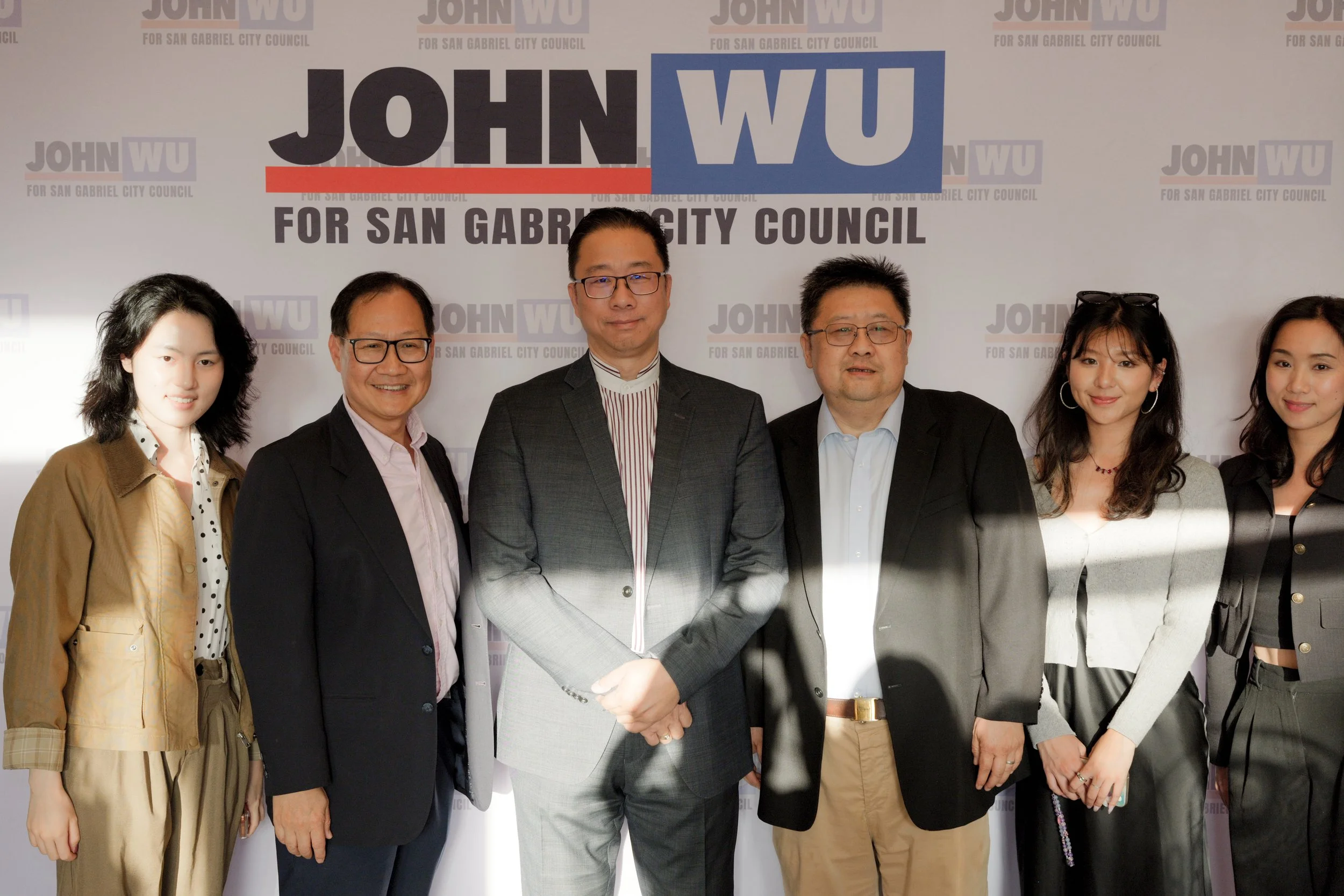 Group photo of seven people standing in front of a campaign backdrop that reads "JOHN WU FOR SAN GABRIEL CITY COUNCIL".