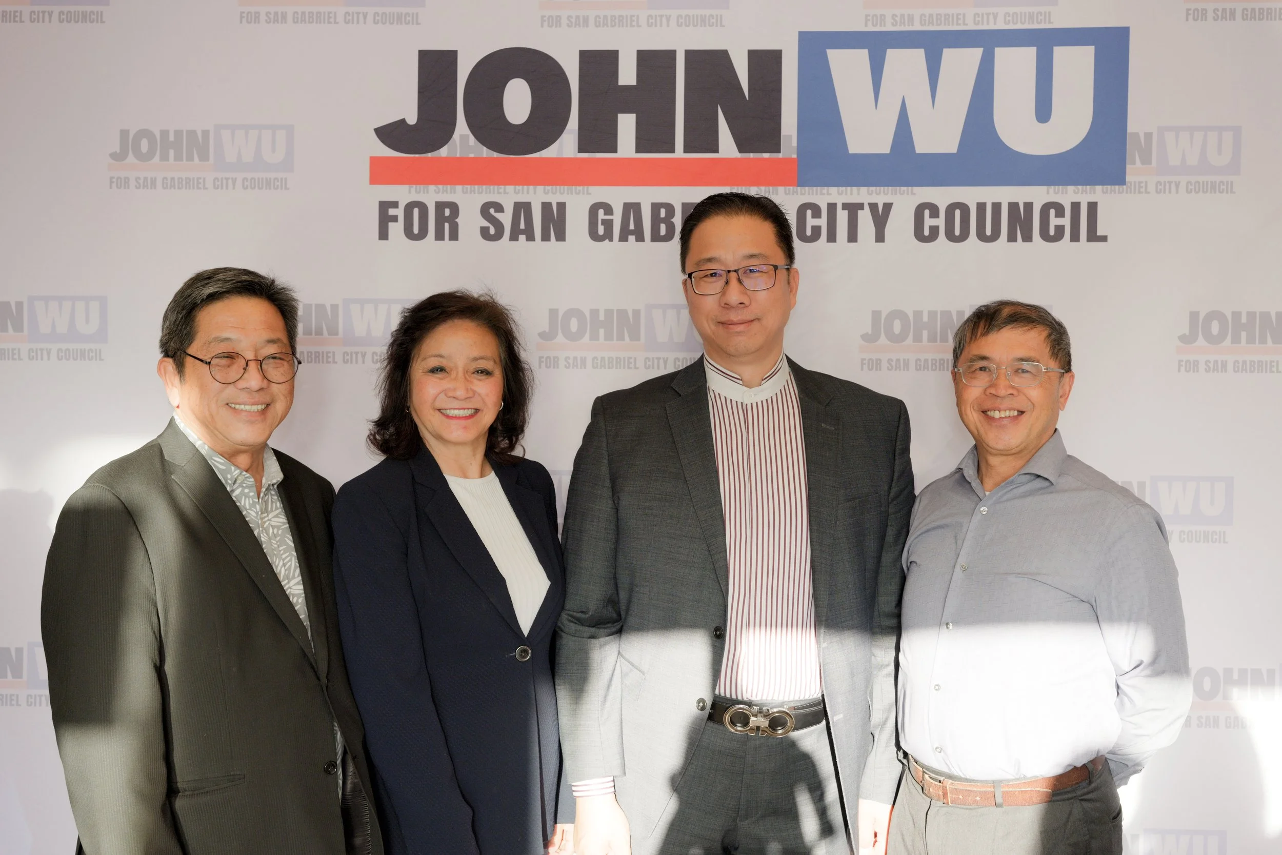 Five people standing in front of a backdrop that says "John Wu for San Gabriel City Council". The group includes two men wearing glasses, one woman, and another man, all smiling.