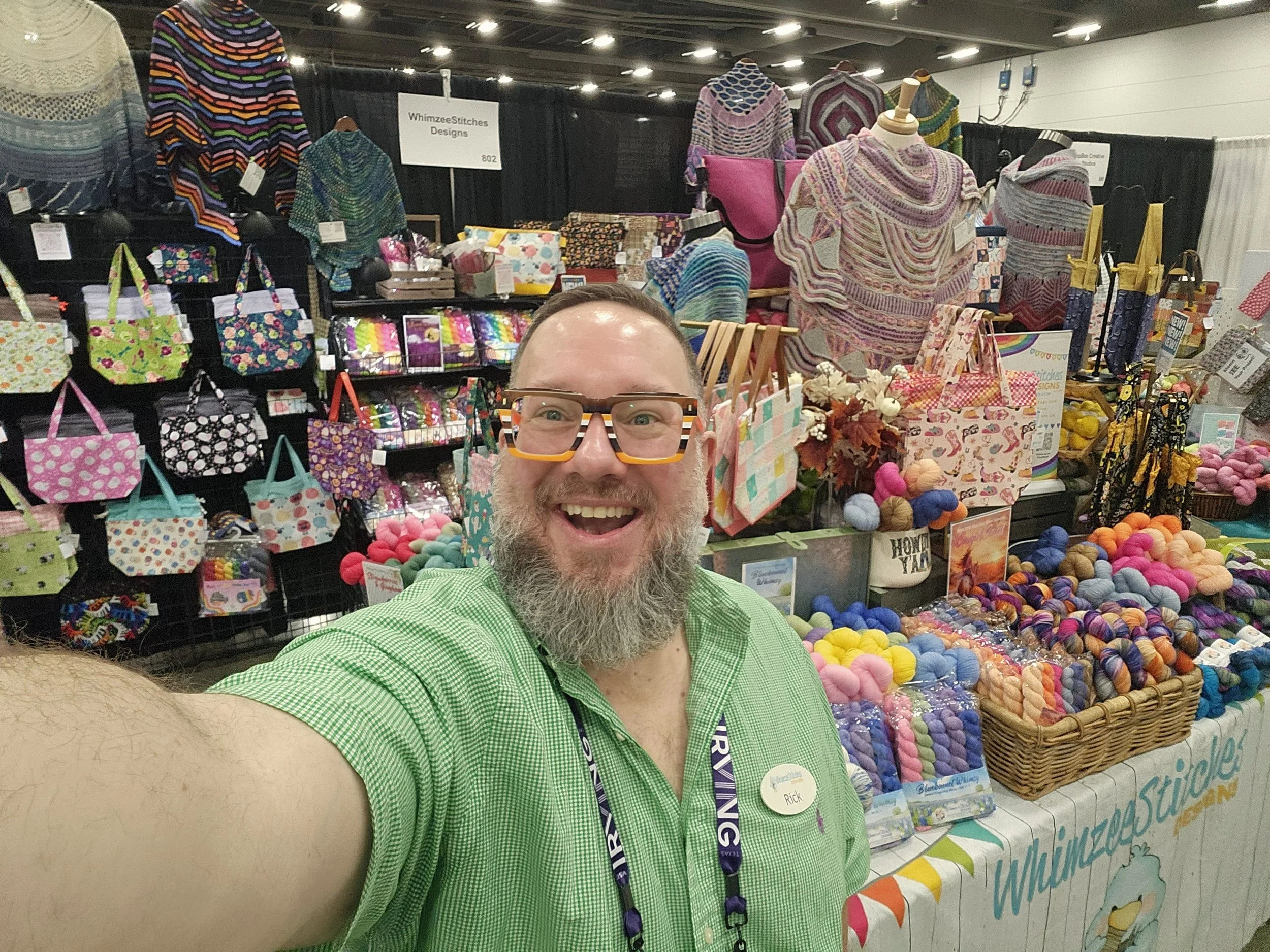 image of Rick Najdzion at DFW Fiber Fest with colorful hand dyed yarns, project bags and hand knit shawls