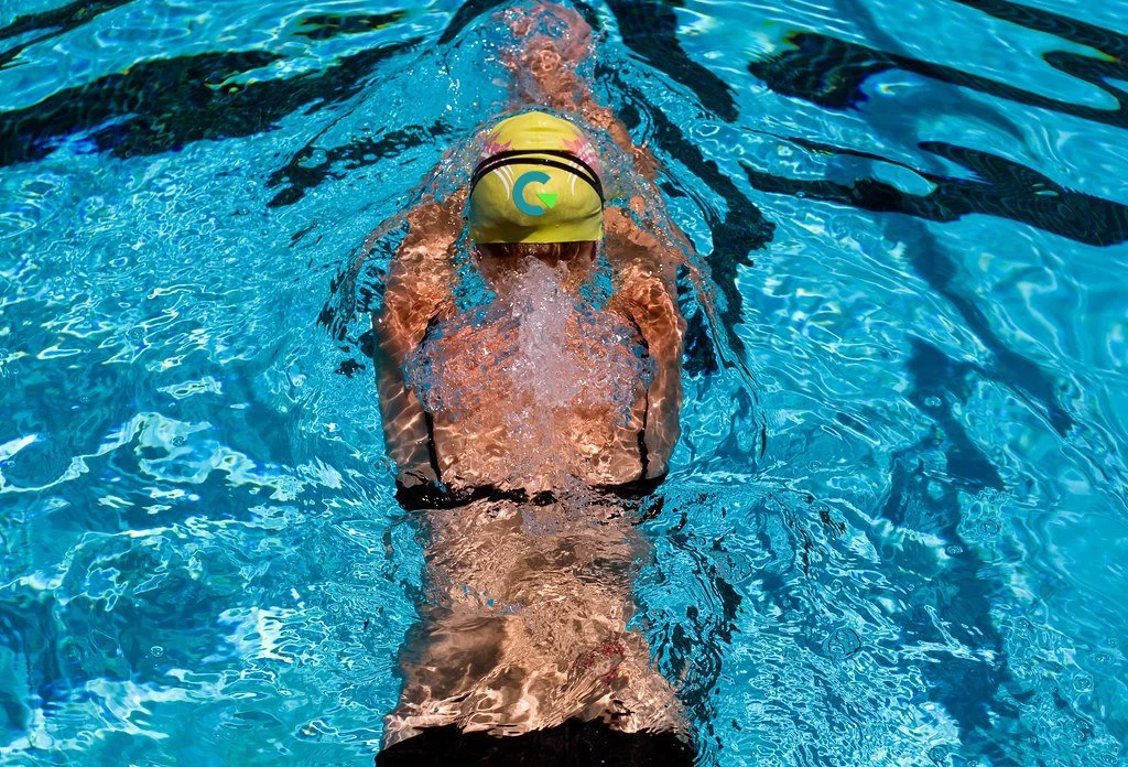 Swimmer wearing yellow swim cap and goggles practicing in a swimming pool.