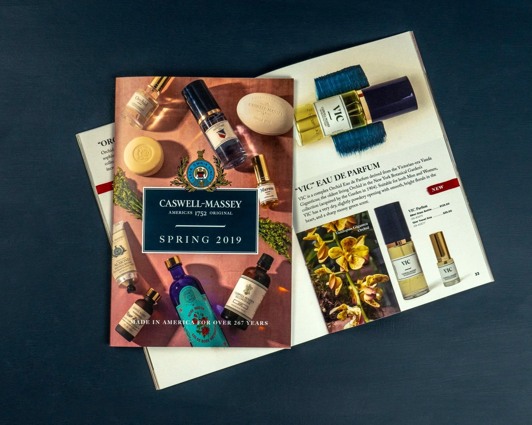 Open magazines displaying Caswell-Massey perfume products with bottles and packaging, on a dark surface.