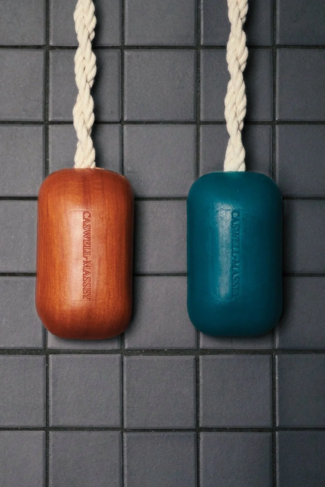 Two gym weights with ropes attached hanging on a tiled wall, one in brown and the other in teal, both engraved with 'Castwell-Massery'.