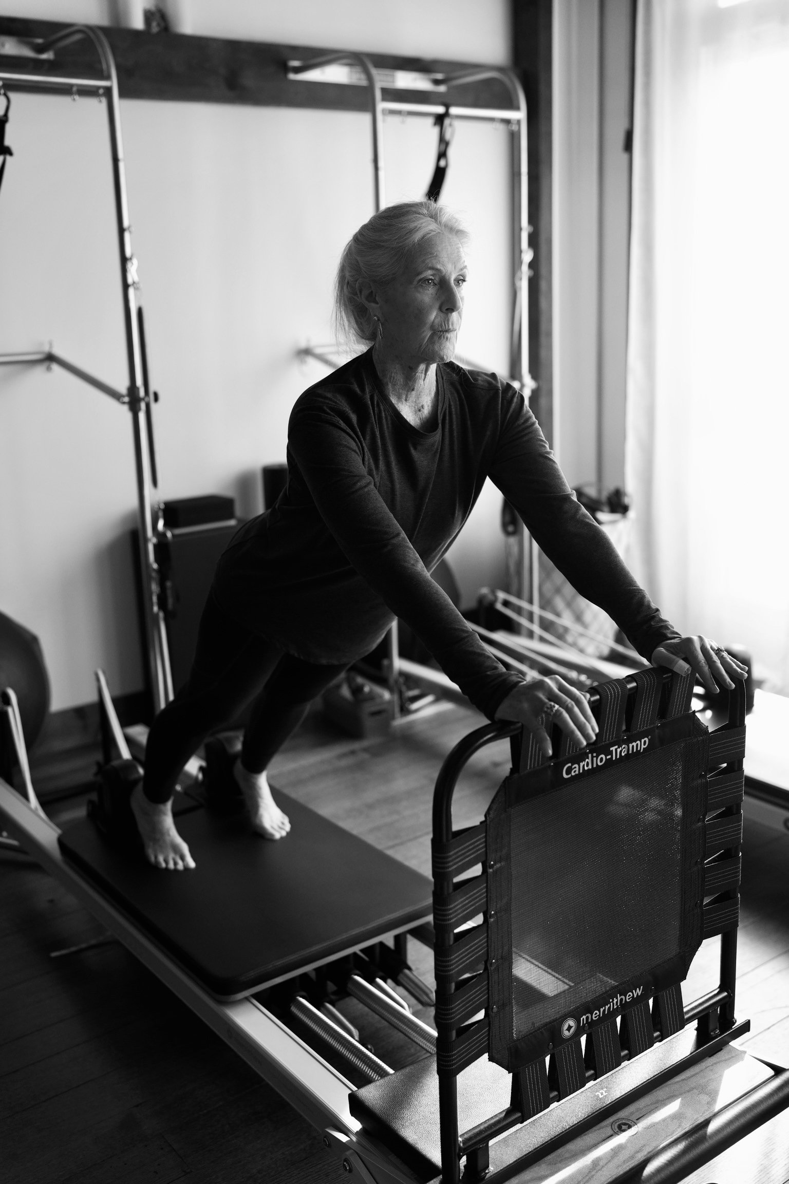 Senior woman exercising on Pilates reformer machine in a gym.
