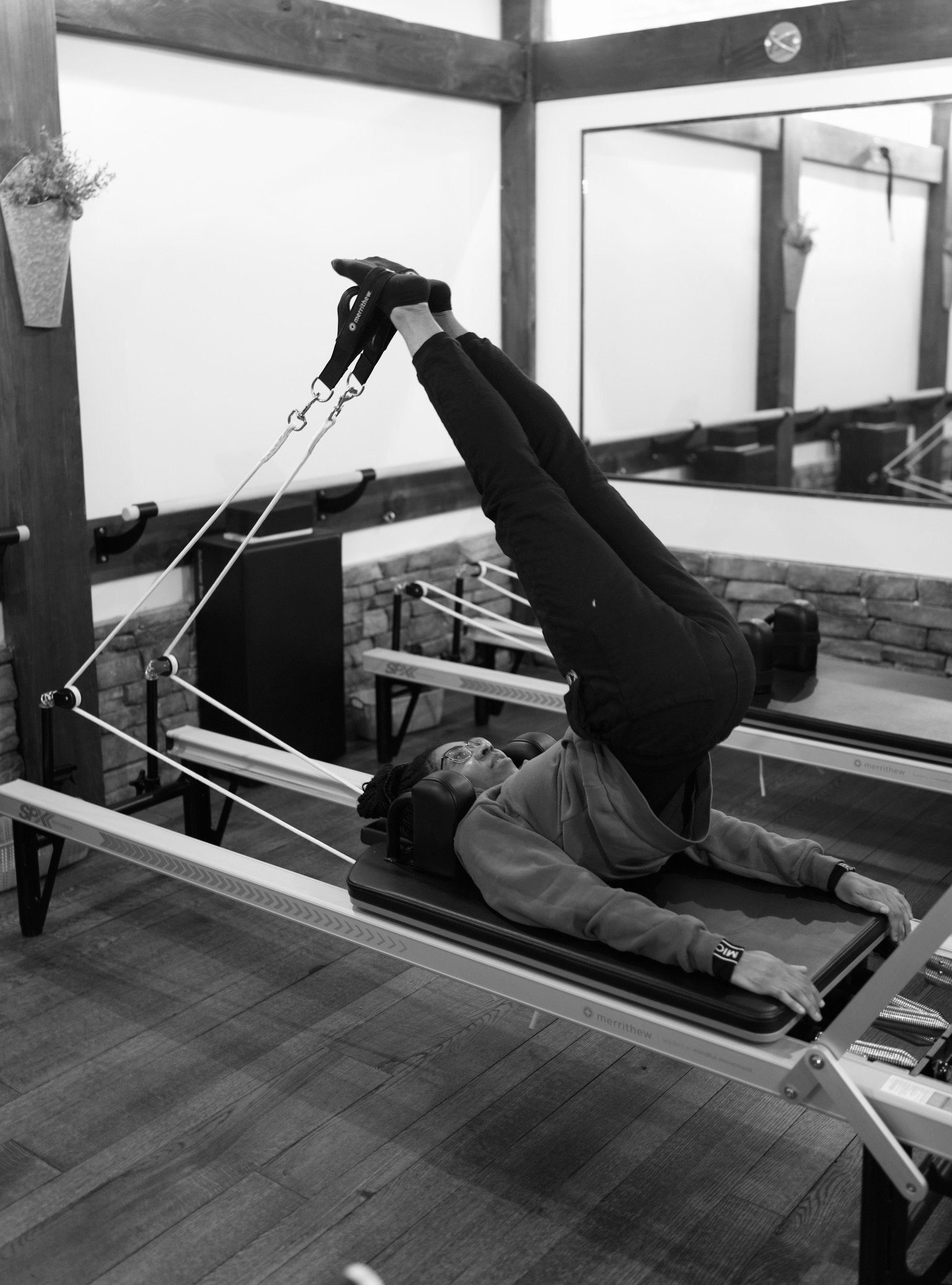 Person exercising on a Pilates reformer machine, performing a yoga pose in a fitness studio.