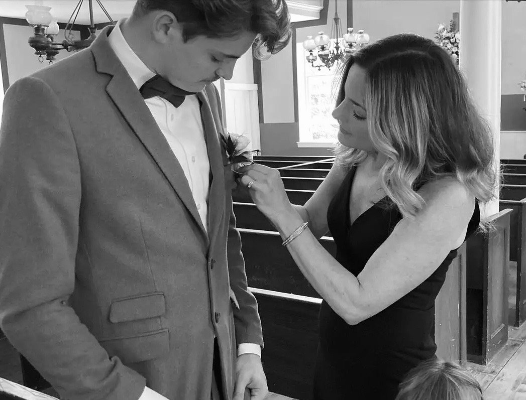 Woman adjusting boutonniere on man in suit inside a church