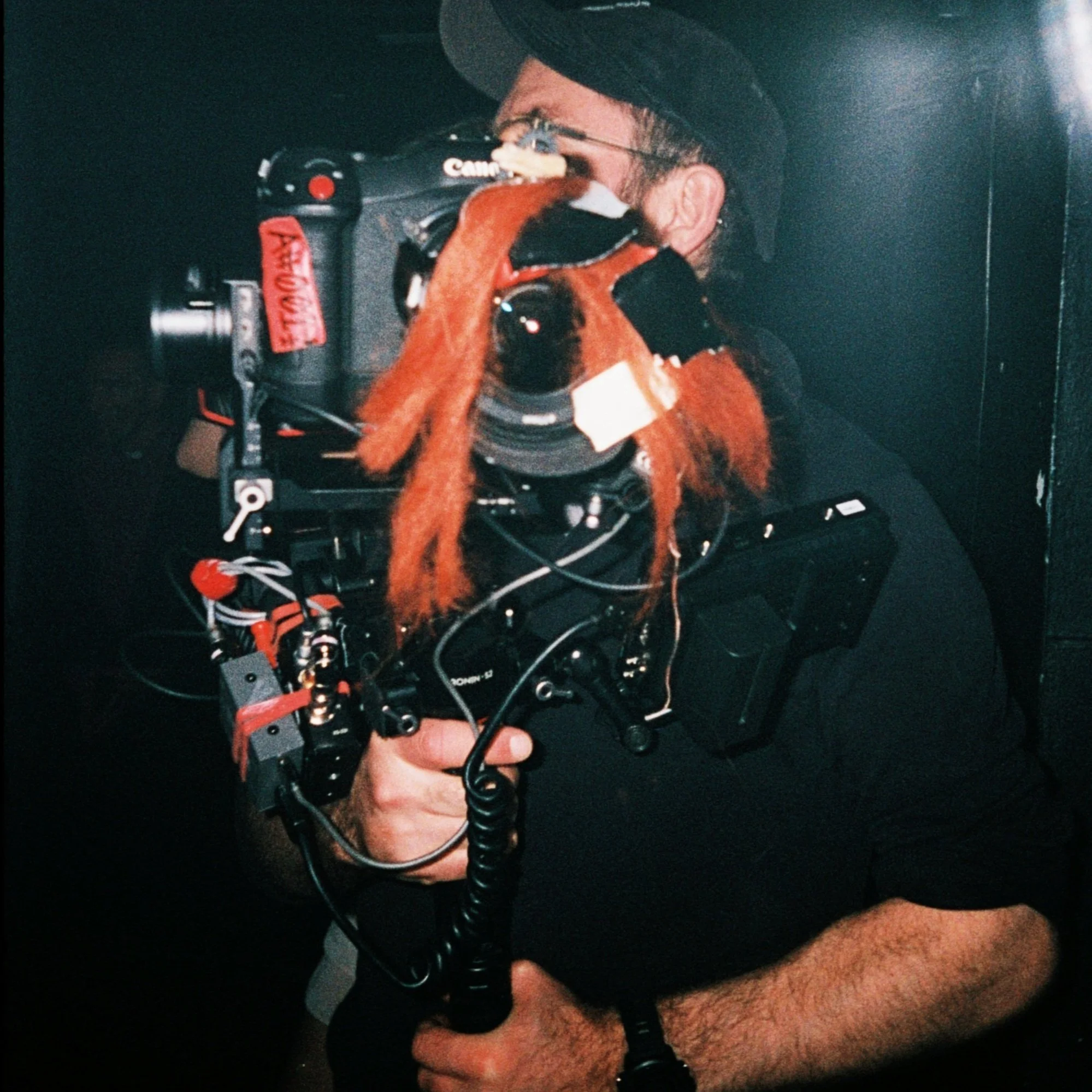 Cinematographer Darren Hercher operating a Canon camera with a large setup, including red furry decorations and various cables in Arab Strap music video Strawberry Moon directed by David Arthur.