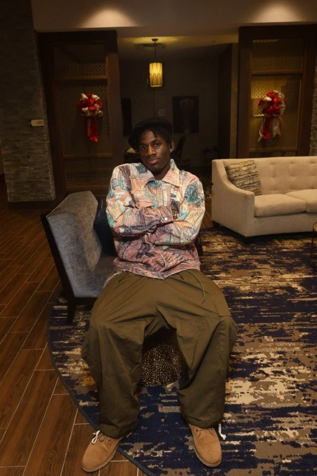 Young man sitting on a chair with crossed arms in a hotel lobby decorated with Christmas wreaths.