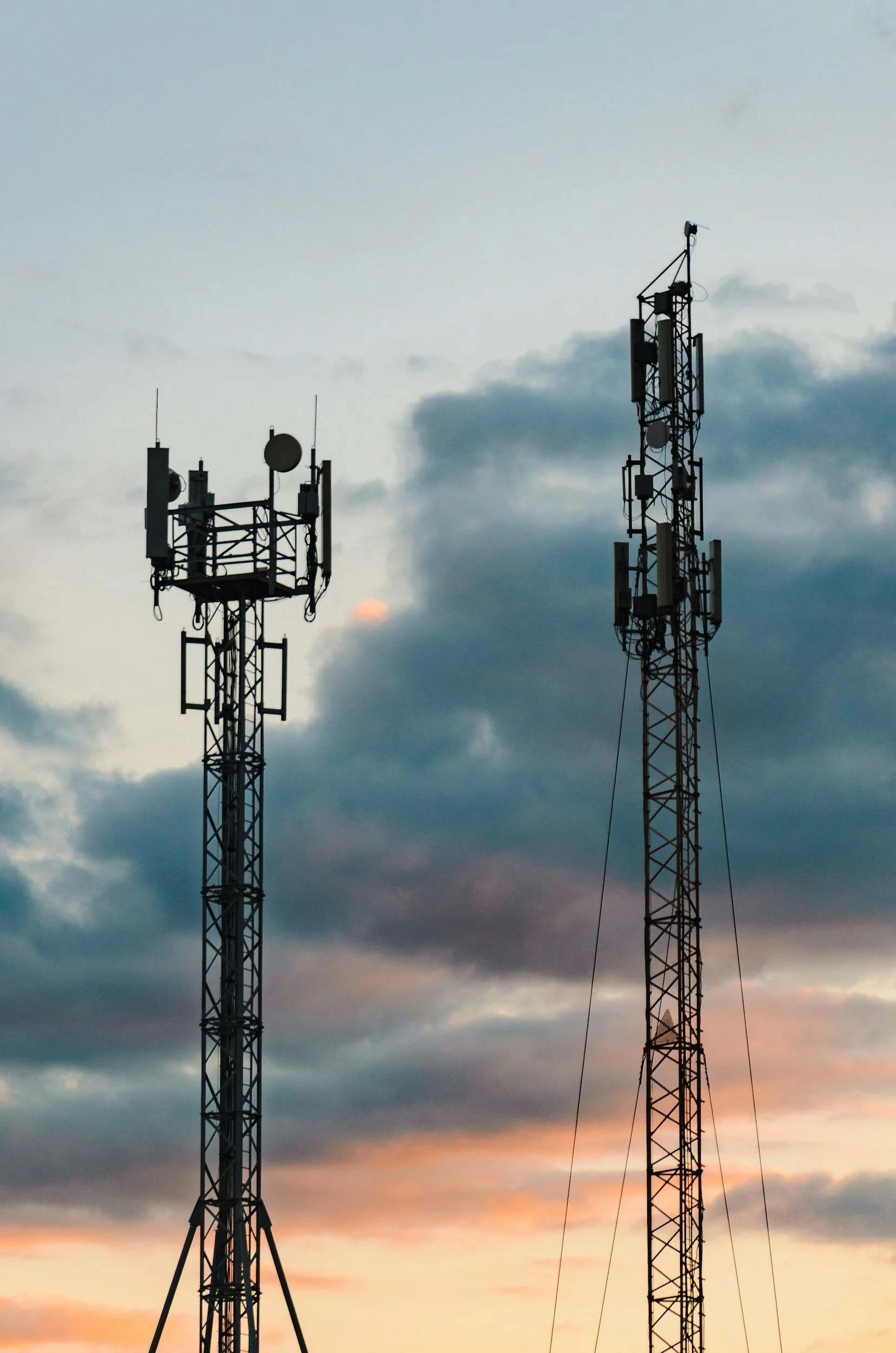 Two telecommunications towers against a cloudy sky