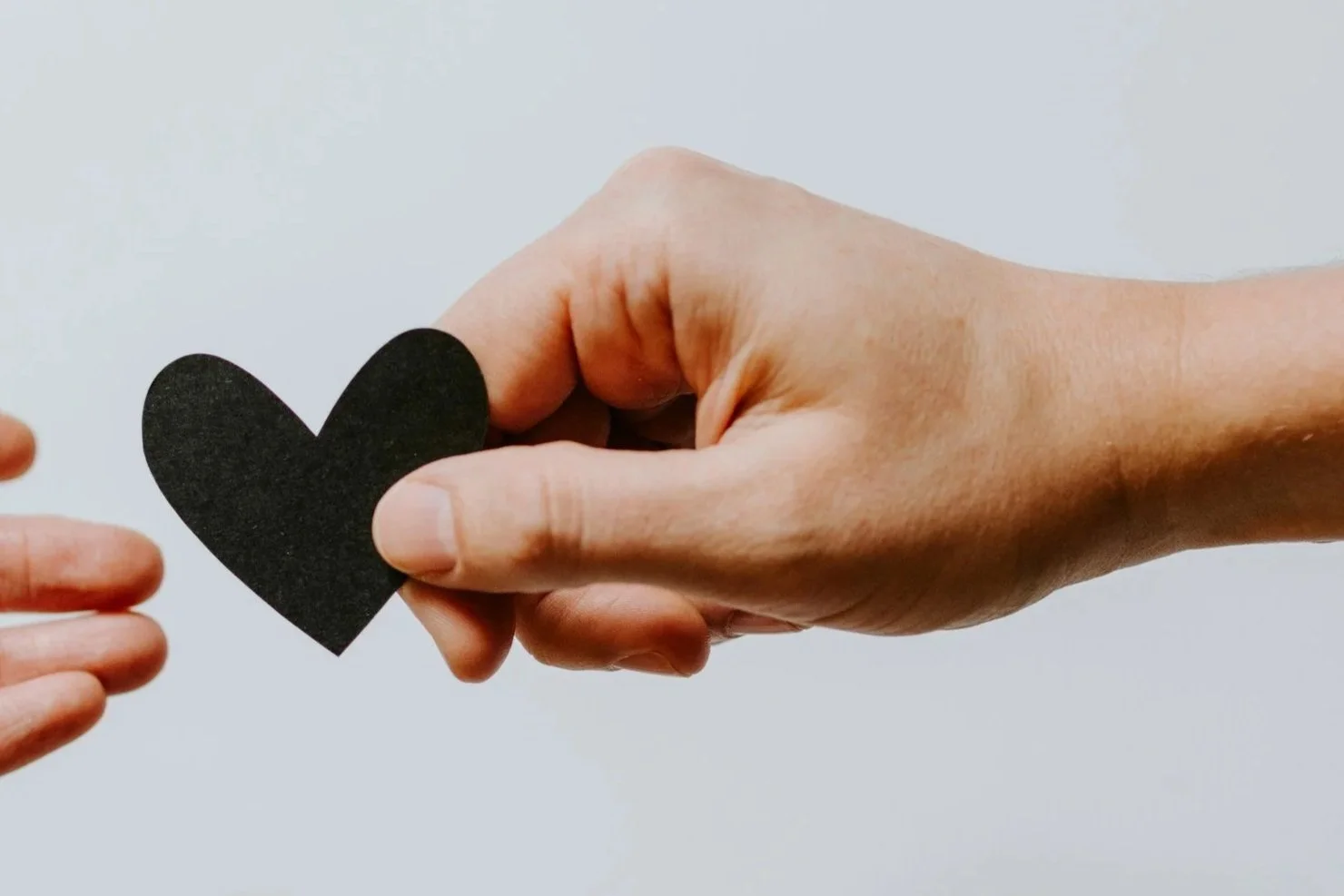 A large hand holding a black heart cutout and offering it to a smaller hand reaching from the left.
