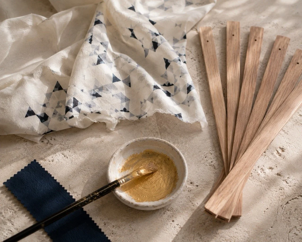 Natural wood, bespoke printed fabric and hand-painted gold details used by Island Whisper Atelier to create luxury handcrafted hand fans for restaurants, hotels and premium brands.