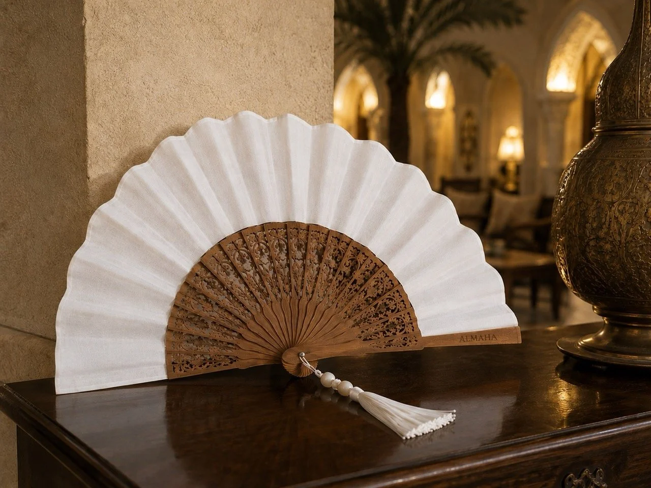 Bespoke luxury hotel hand fan by Island Whisper Atelier with intricate carved wood, white fabric, custom engraving and luxury tassel with natural stone, designed for Middle East hospitality.