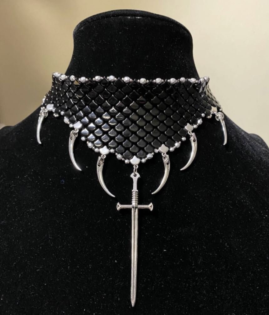 Black velvet jewelry bust displaying a tall and ornate black Czech glass dragon scale choker with long curved spike charms flanking a long sword