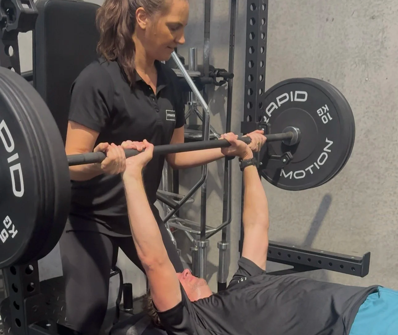 A woman leaning over supporting someone to do a bench press