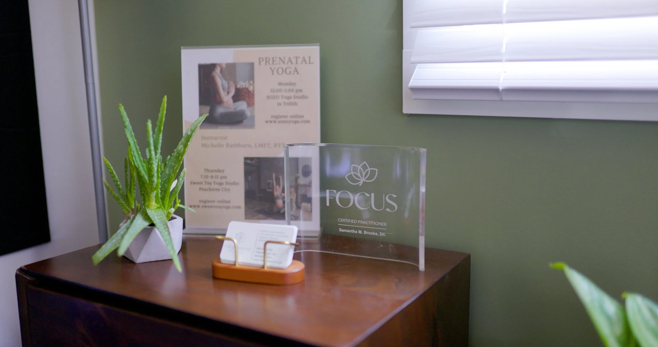 Office corner with aloe plant, yoga class flyer, business cards, and Focus Practitioner award.