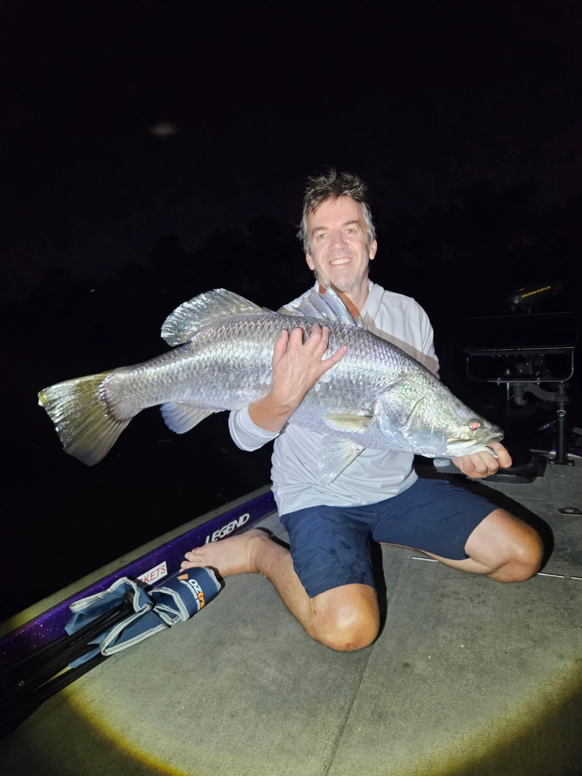 Man kneeling on a boat at night, holding a large fish.