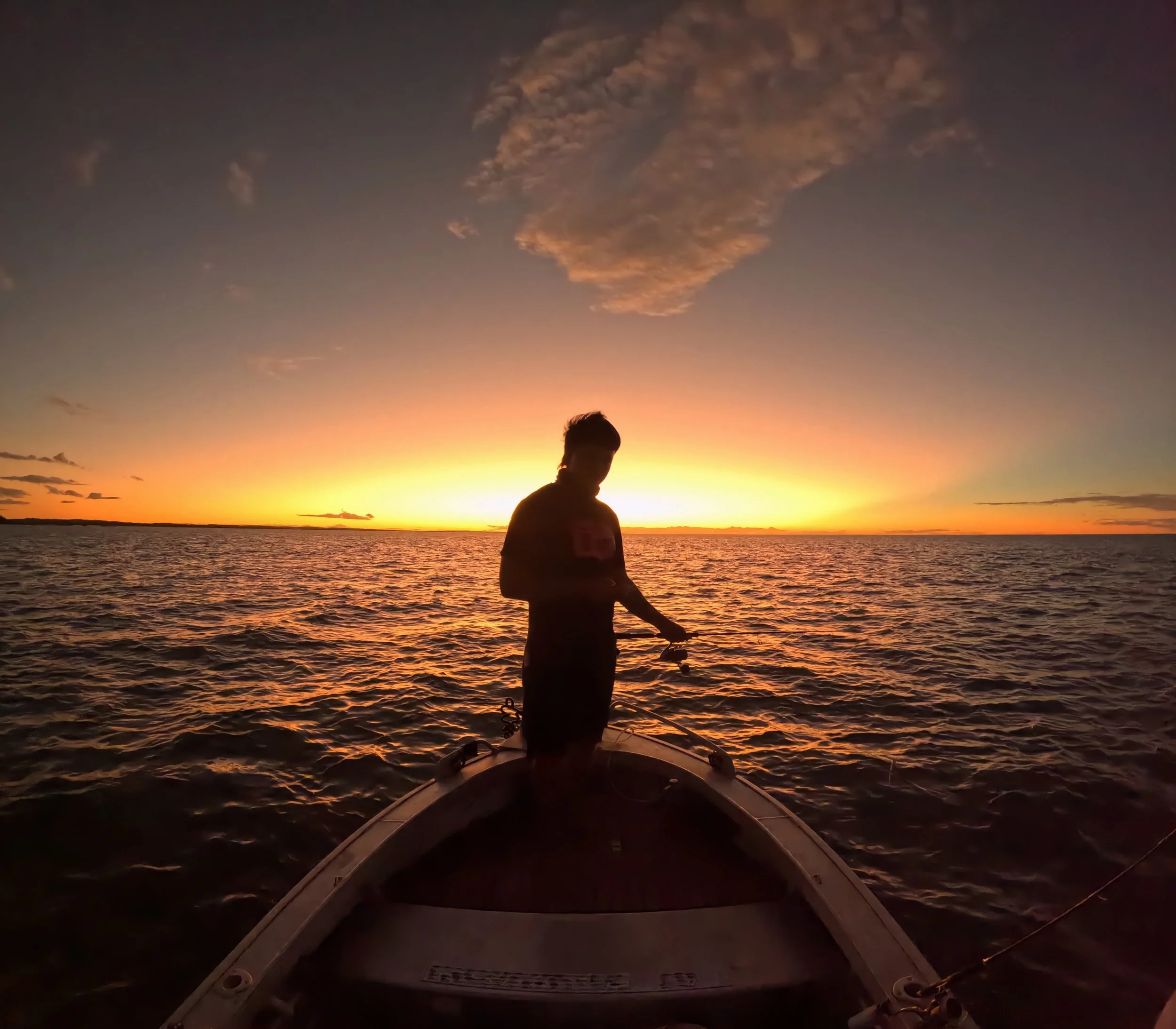 Person standing on a boat at sunset over the water.