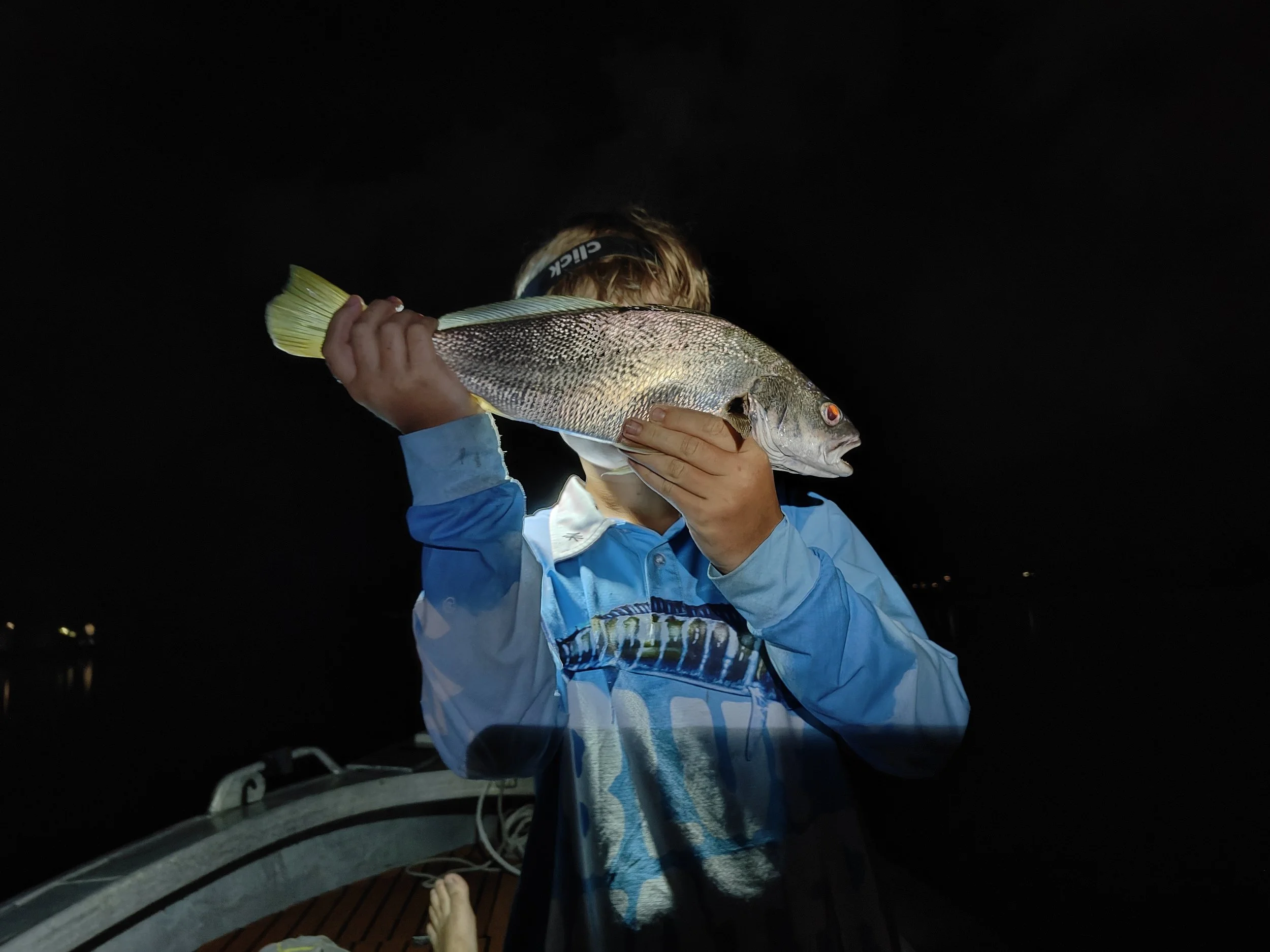 Person holding a large fish at night on a boat.