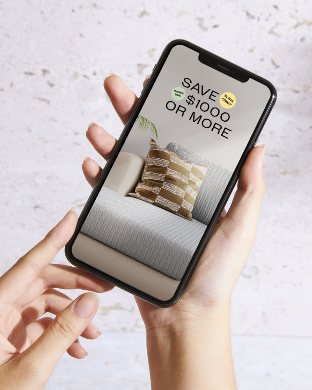 Hand holding a smartphone displaying a home decor sale advertisement with a beige sofa and pillows.