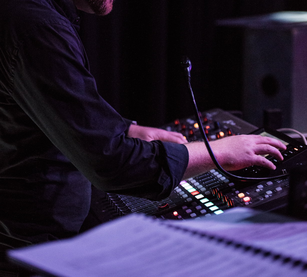 A DJ performs at a dark venue, using a digital mixing console with colorful illuminated buttons and sliders.